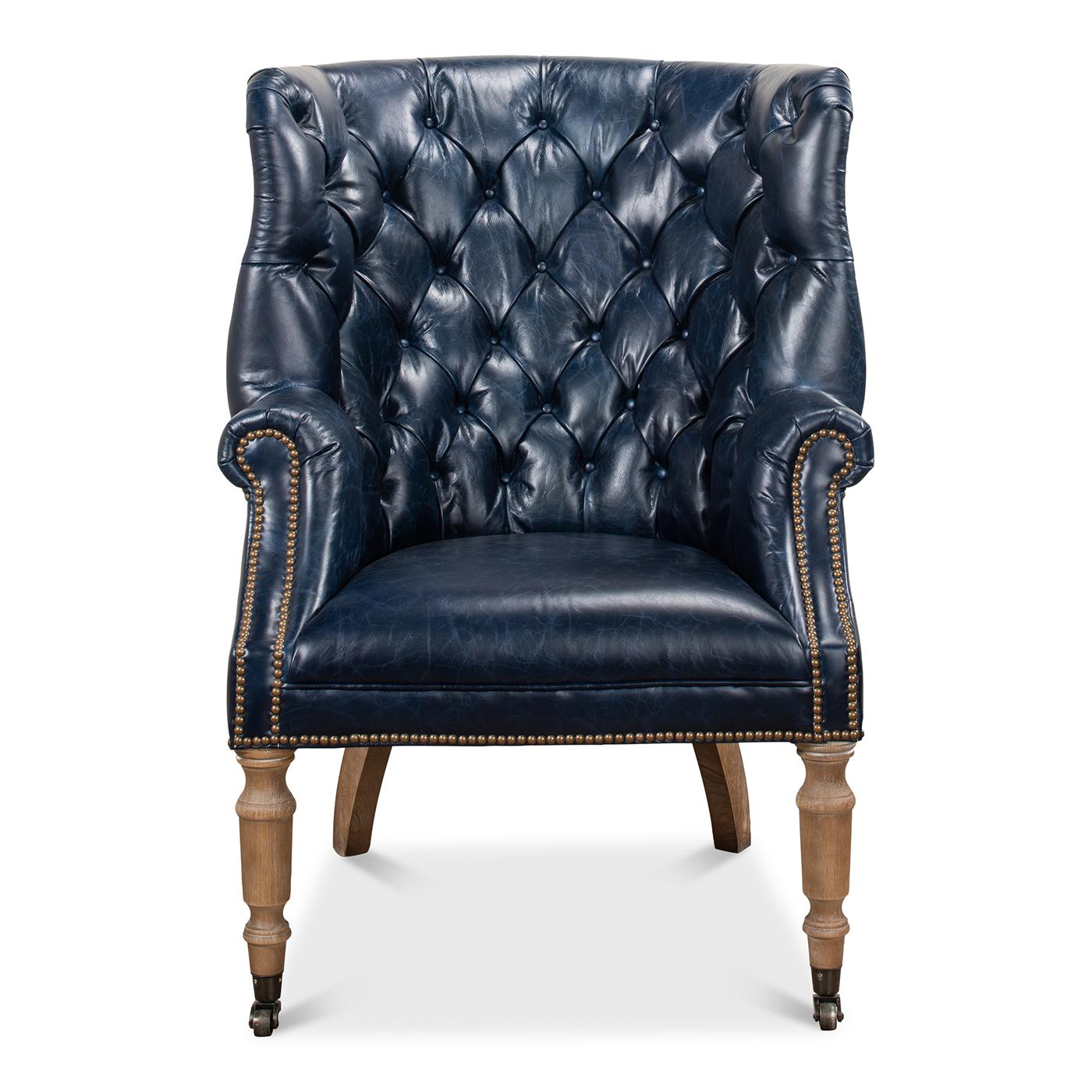 A wonderful George III style barrel back wingchair with top-grain Chateau blue colored leather, a tufted upholstery barrel backrest with winged sides, rolled arms and a padded seat. Finished with brass nailhead trim and raised on cerused turned