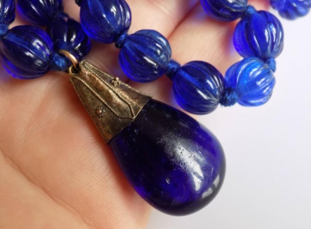 Un rare collier de perles de verre bleu fait à la main en Géorgie avec pendentif. Pendentif en monture d'argent, avec raccords en or rose. Un collier qui attire l'attention. Origine anglaise. 
Perles de 8mm à 9mm. 
Hauteur du pendentif 40 mm,