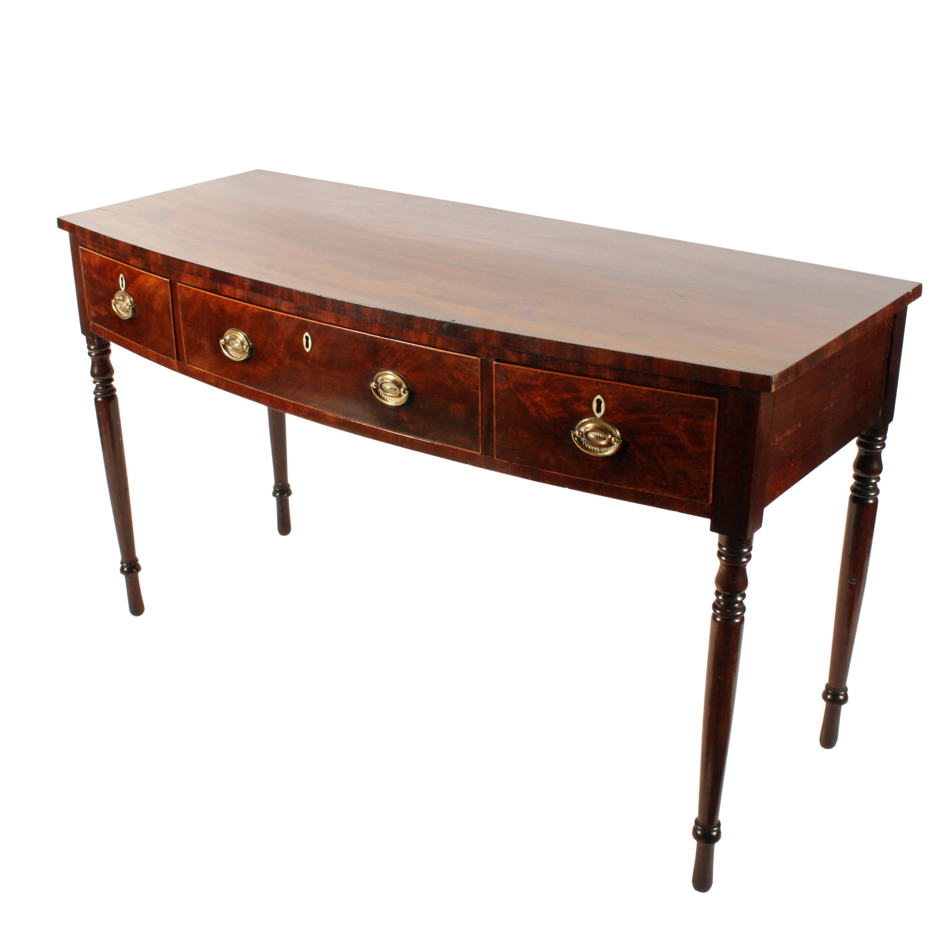 An early 19th century Georgian mahogany three-drawer bow front side table.

The table has a square top edge and stands on four tapering turned mahogany legs.

The three bow fronted drawers have a box wood edge, original oval brass handles and