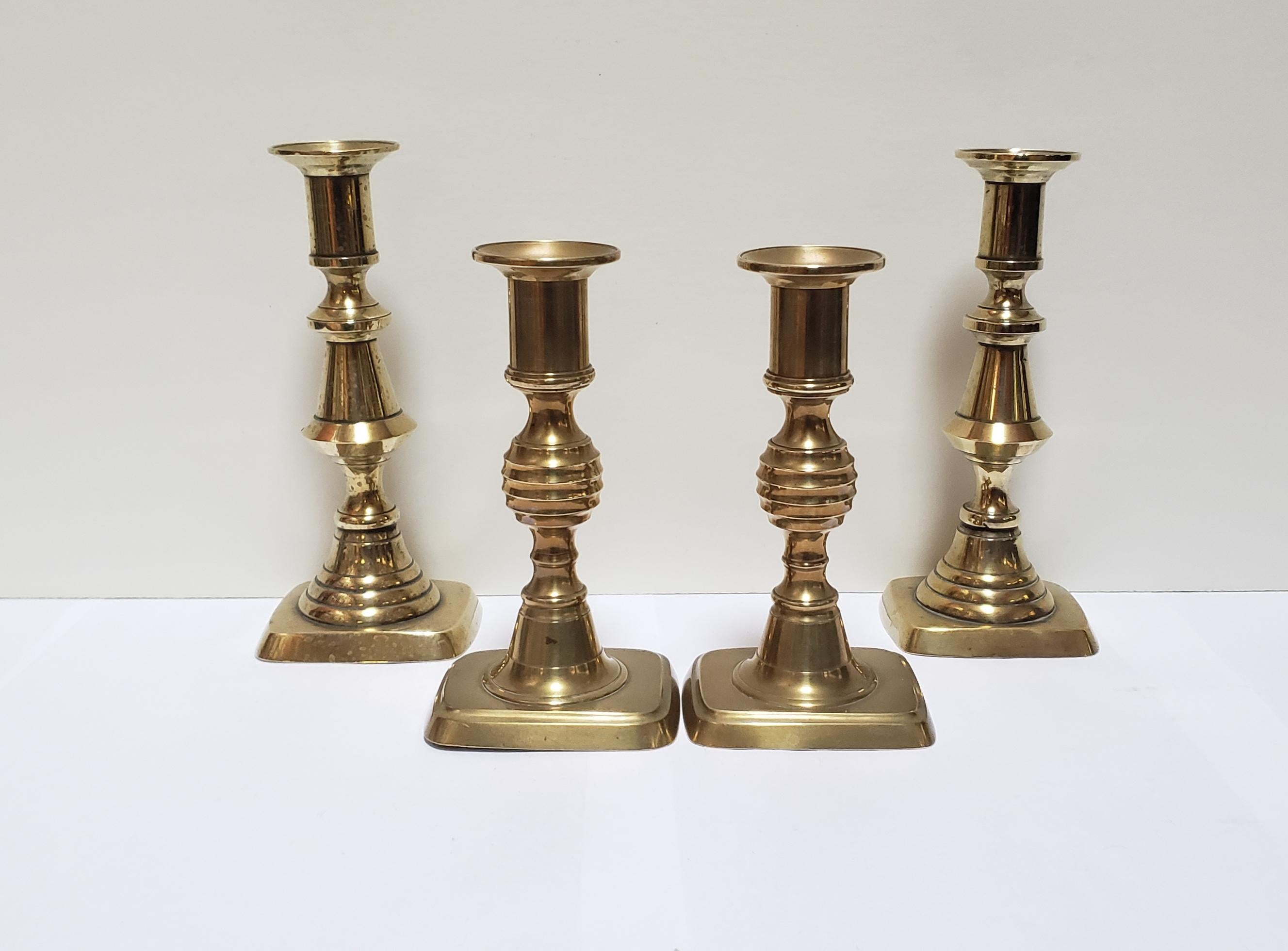 2 pairs of rectangular base, pull-up brass English candlesticks from the period of George IV (reign 1820-1830). The taller pair have a baluster turned pedestal while the shorter pair have a beehive knobbed pedestal. Both pairs have their original