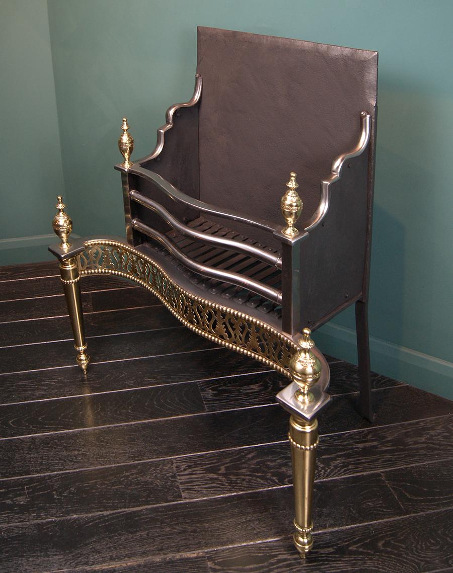 A beautiful Georgian brass and steel dog grate. The railed basket with fine engraved openwork fret consisting of scrolls and foliage, set on turned brass legs with engraved vase finials uppermost. The rear elements consist of a rivet-work grill and