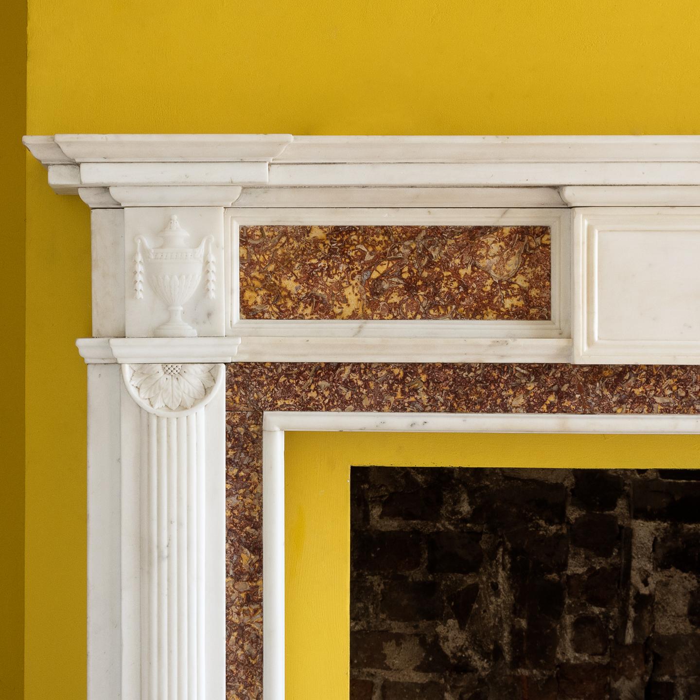 A George III Brocatello and statuary marble chimneypiece, the inverse breakfront moulded shelf above frieze centered by plain paneled tablet, the flanking endblocks with classical urns on reeded jambs surmounted by half paterae, with brocatello in