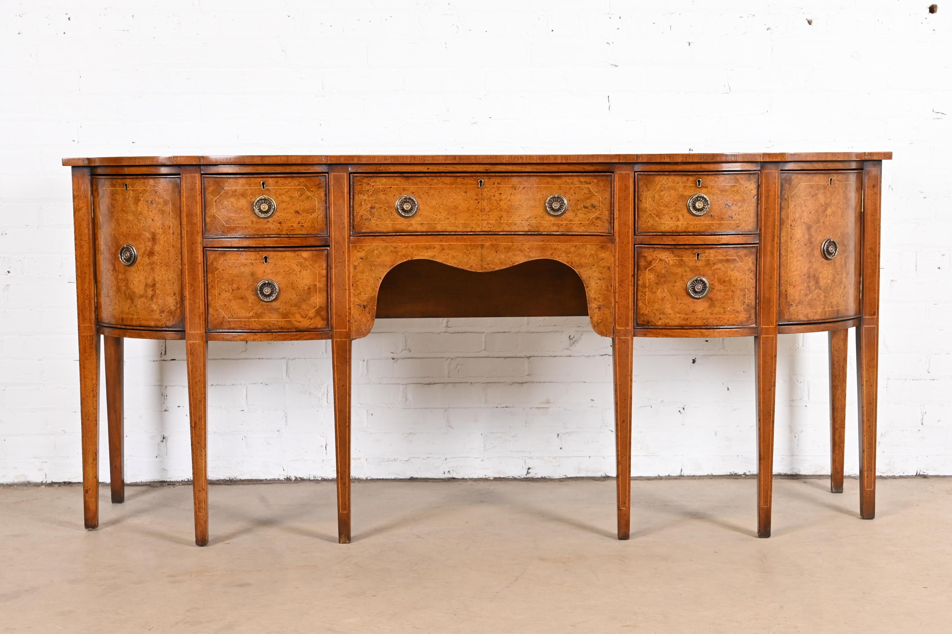 A gorgeous antique Georgian or Hepplewhite style double serpentine sideboard or credenza

In the manner of Baker Furniture

USA, circa 1930s

Beautiful burled walnut, with satinwood string inlay, and original brass hardware.

Measures:
