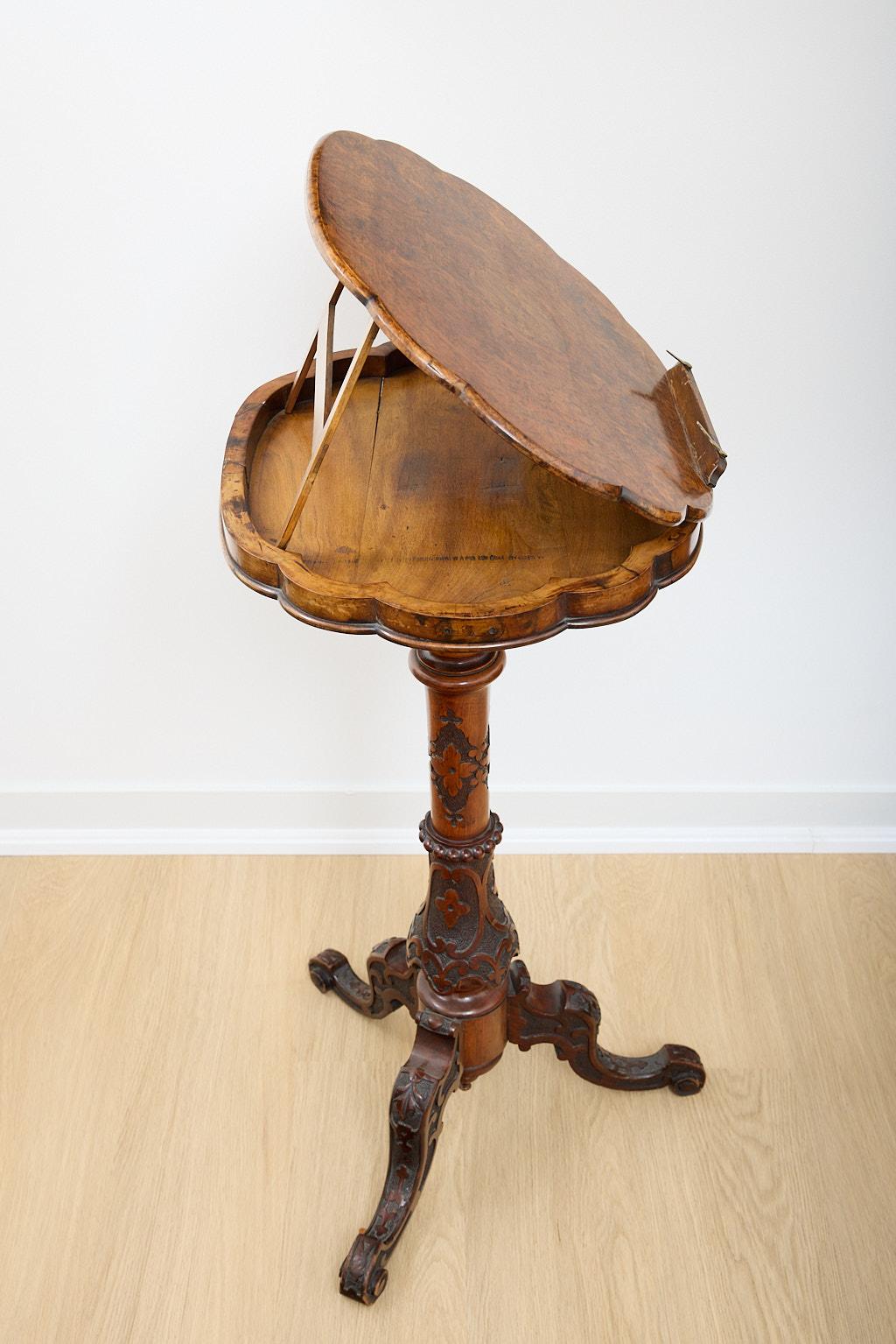 Petite Burled walnut bookstand. This lovely table has a scalloped oval surface in burled walnut. It is raised on a central carved wood post terminating in cabriole legs with scroll feet. Possibly Irish. 
This piece can be raised or lowered through