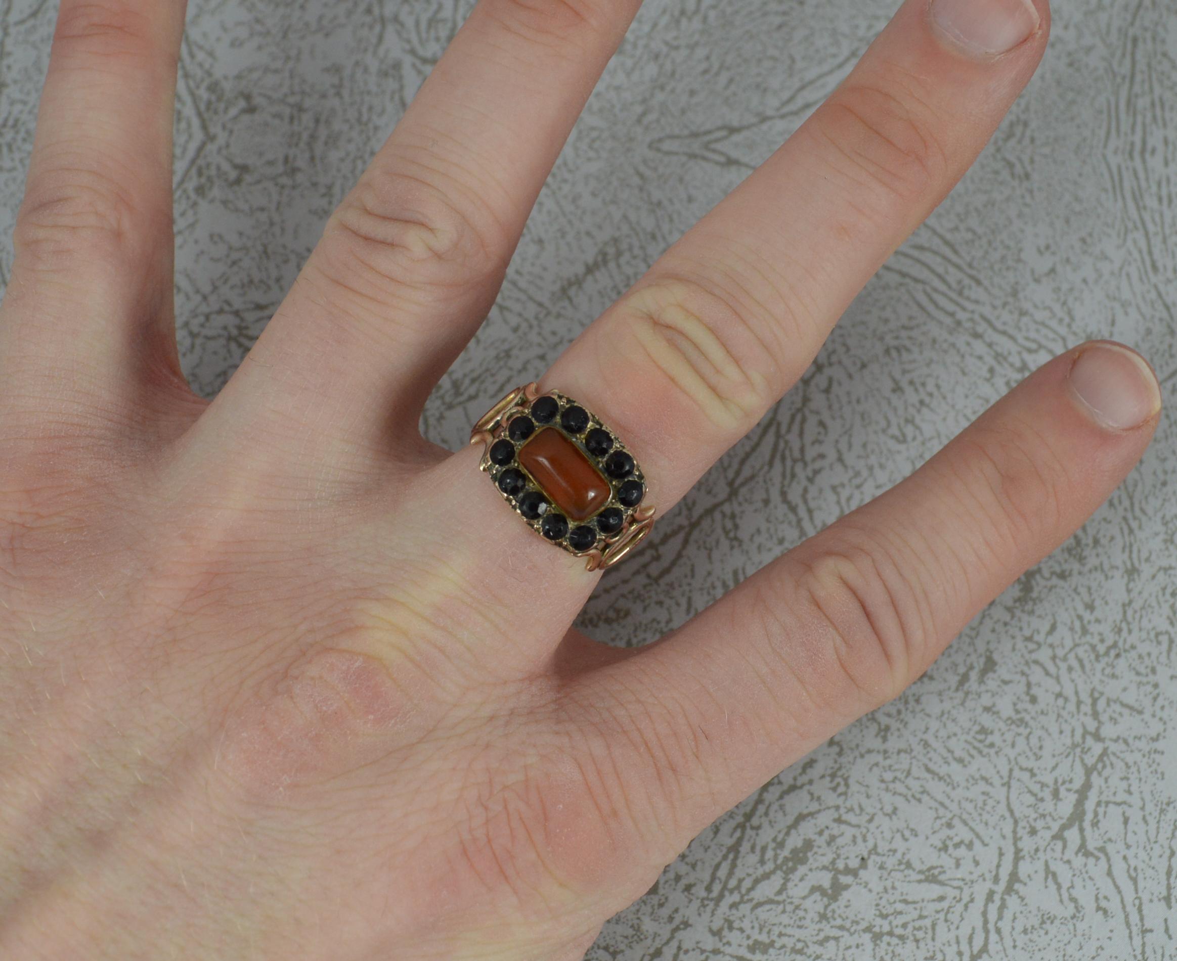 A true Georgian period cluster ring. c1820.
Designed with a carnelian to the centre with twelve round onyx stones surrounding and a pierced oval shoulder design.
Solid 9 carat rose gold example.
12mm x 15mm head.

CONDITION ; Very good for age.