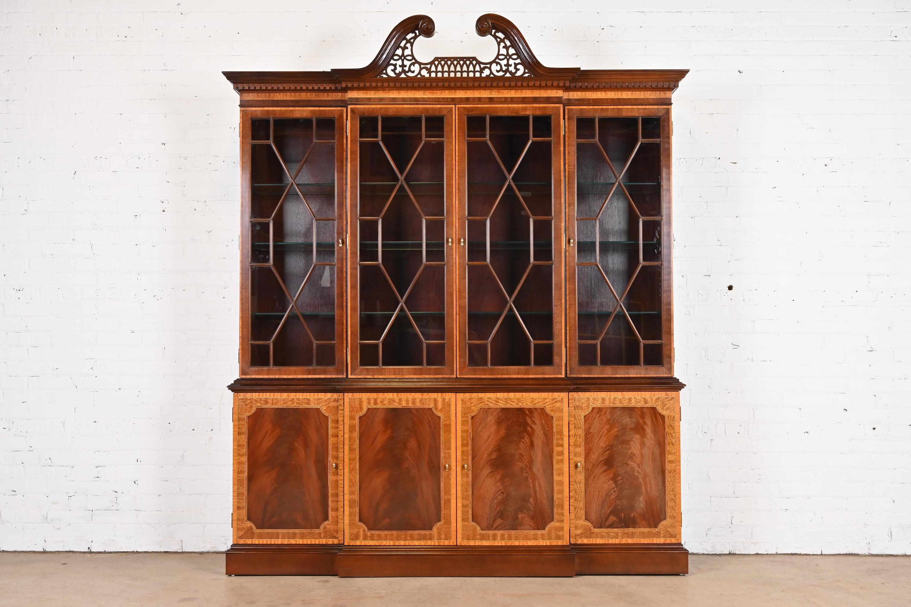 A gorgeous Georgian or Chippendale style lighted breakfront bookcase or dining cabinet

In the manner of Baker Furniture

By Craftique

USA, Circa 1980s

Carved mahogany with satinwood banding, mullioned glass front doors, and original brass