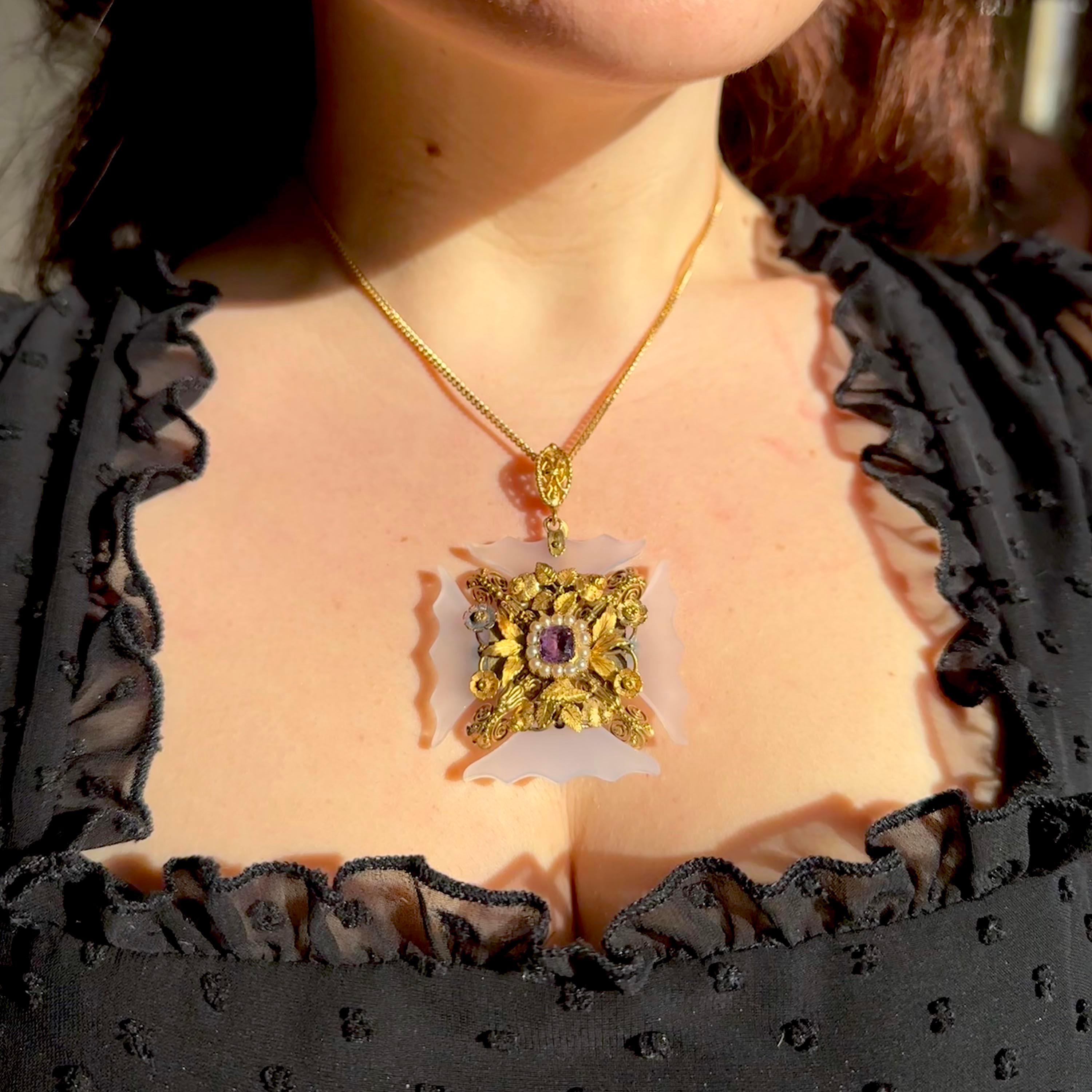 Una croce pattée georgiana, con un'ametista sfaccettata a forma di cuscino incastonata al centro, con un contorno di mezze perle naturali, in una montatura delicata in argento dorato e oro 15 ct, con fiori individuali, foglie, volute e granulazione,