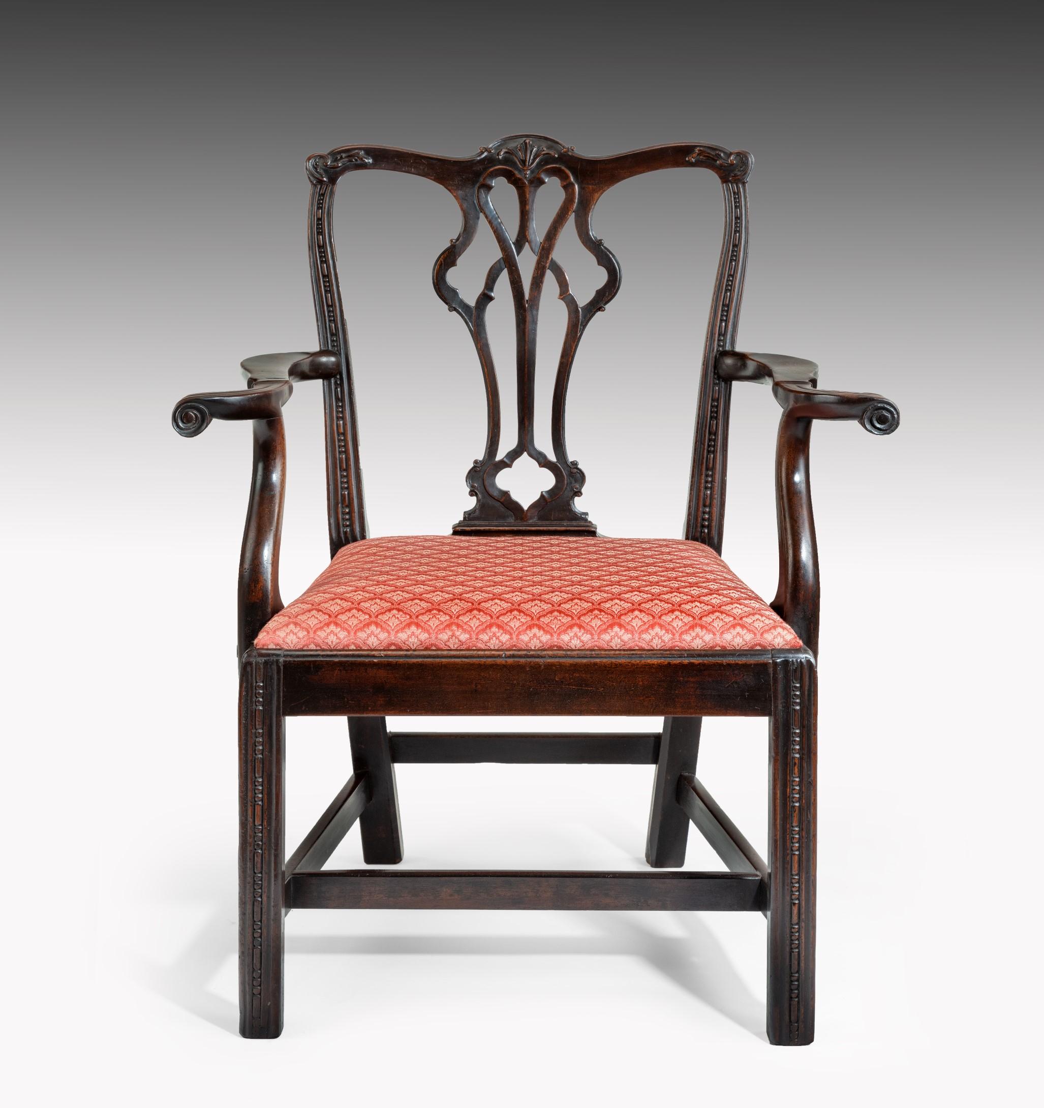 A George III Chippendale period mahogany armchair; the scrolling top rail carved with a central acanthus leaf above a pierced splat and bold outscrolling arms. The armchair has an upholstered drop-in seat and is raised on square moulded legs which