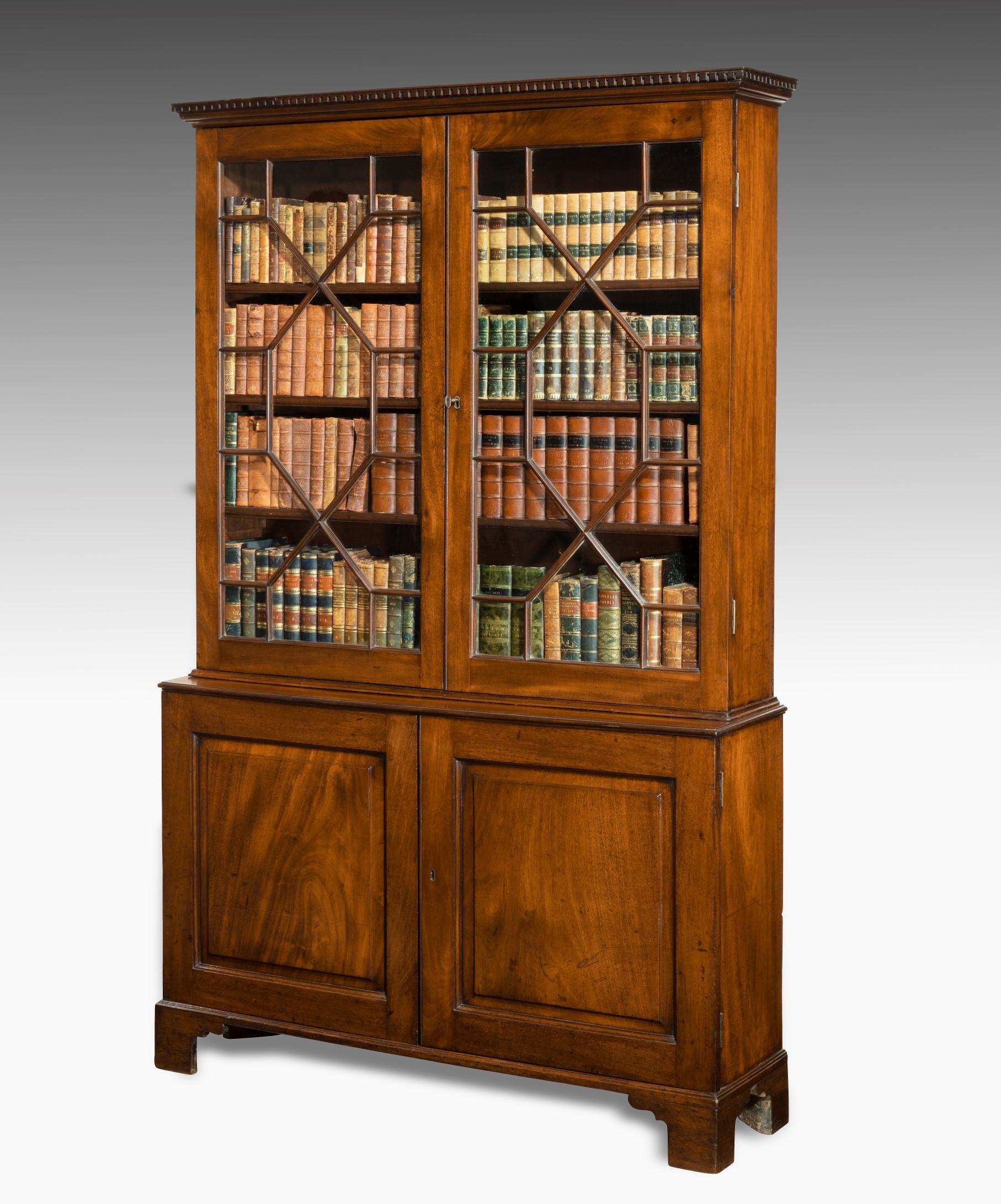 A George III Chippendale period mahogany cupboard base bookcase; the bookcase's dentil moulded cornice above a pair of thirteen pane astragal glazed doors which open to reveal fully adjustable bookshelves; below is a pair of fielded panel cupboard