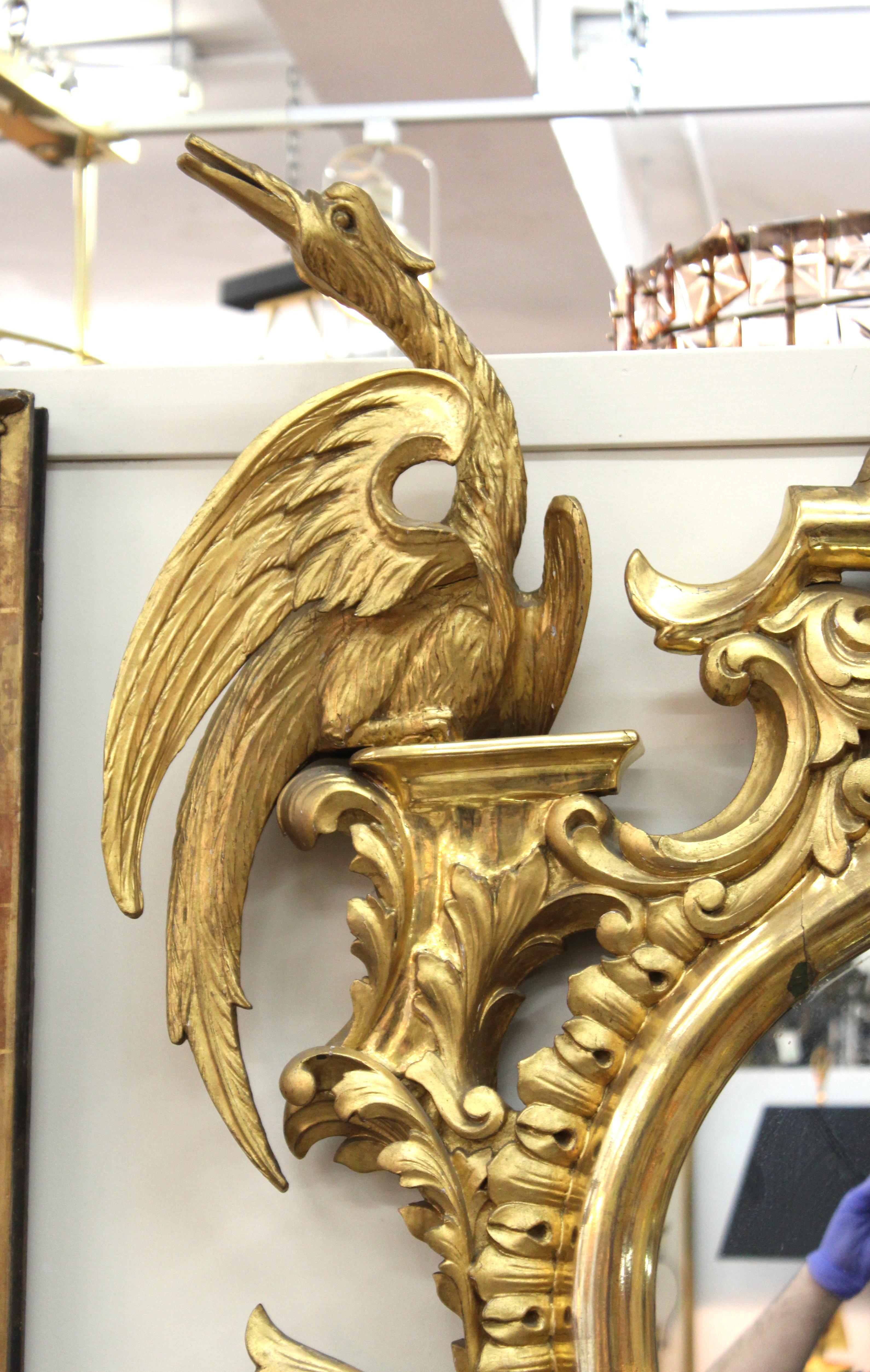 English Georgian carved giltwood mantel mirror in the Rococo style of Chippendale. The mirror features an oblong oval surrounded by an abundance of scrolls and foliage as well as a pair of mythological Asian ho ho birds. In great antique condition