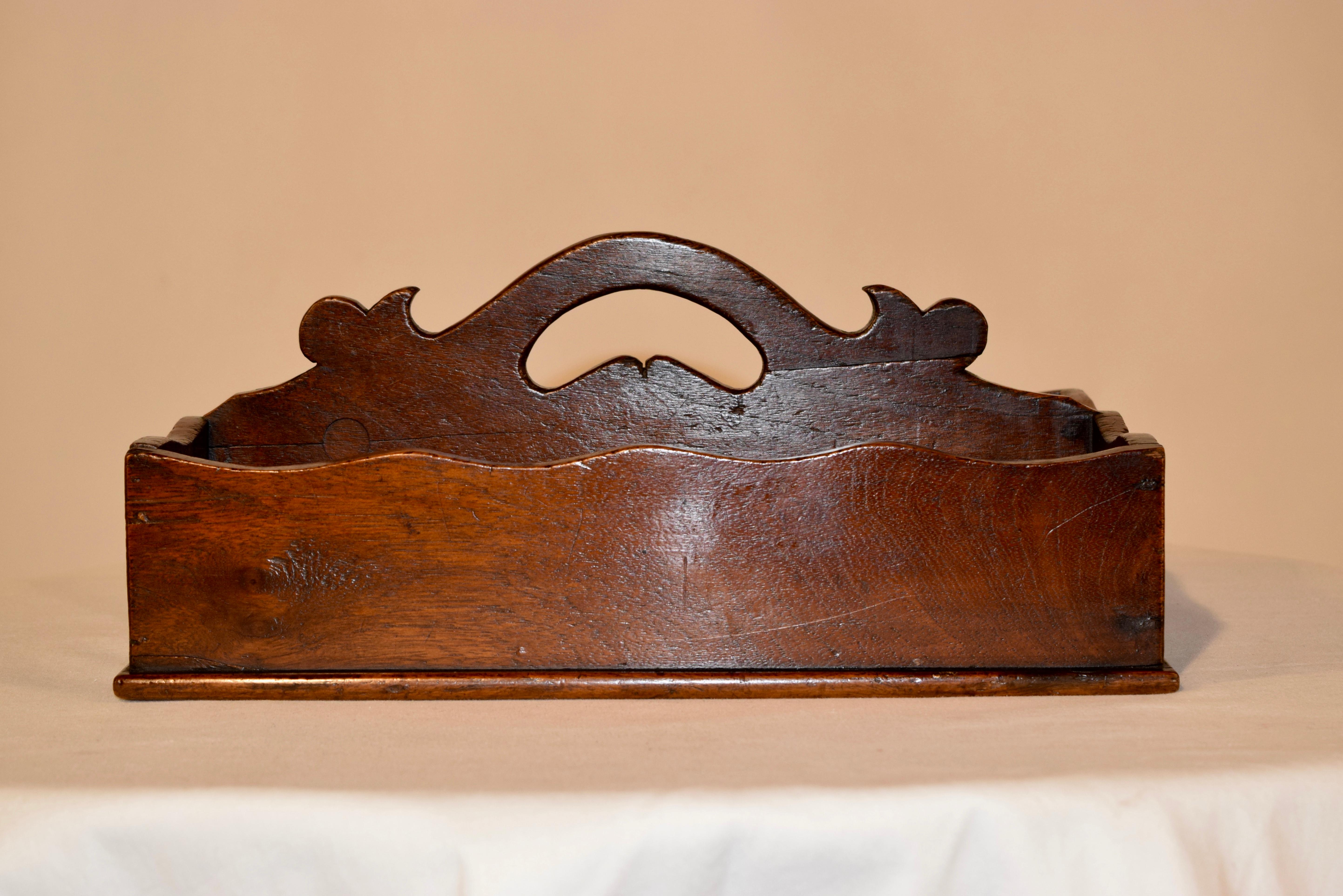 Georgian oak cutlery caddy from England. The handle has hand scalloped and shaped elements, as well as the scalloping around the top rim of the caddy. It has two sections, and is resting on a solid base.