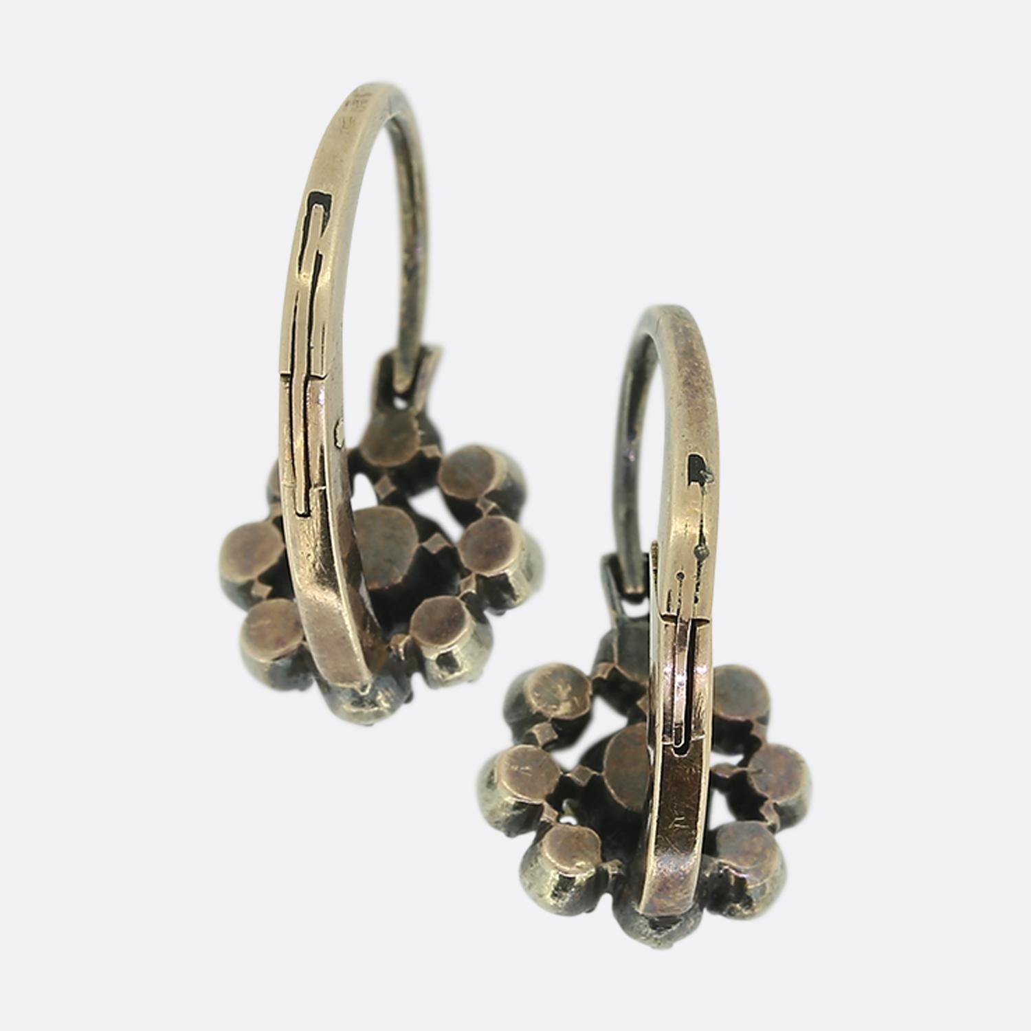 Here we have a pair of drop earrings featuring old mine cut diamonds. Each identical piece showcases a centralised stone surrounded by a halo of smaller diamonds, all set in a delicate arrangement. The diamonds exhibit a captivating colour tone,