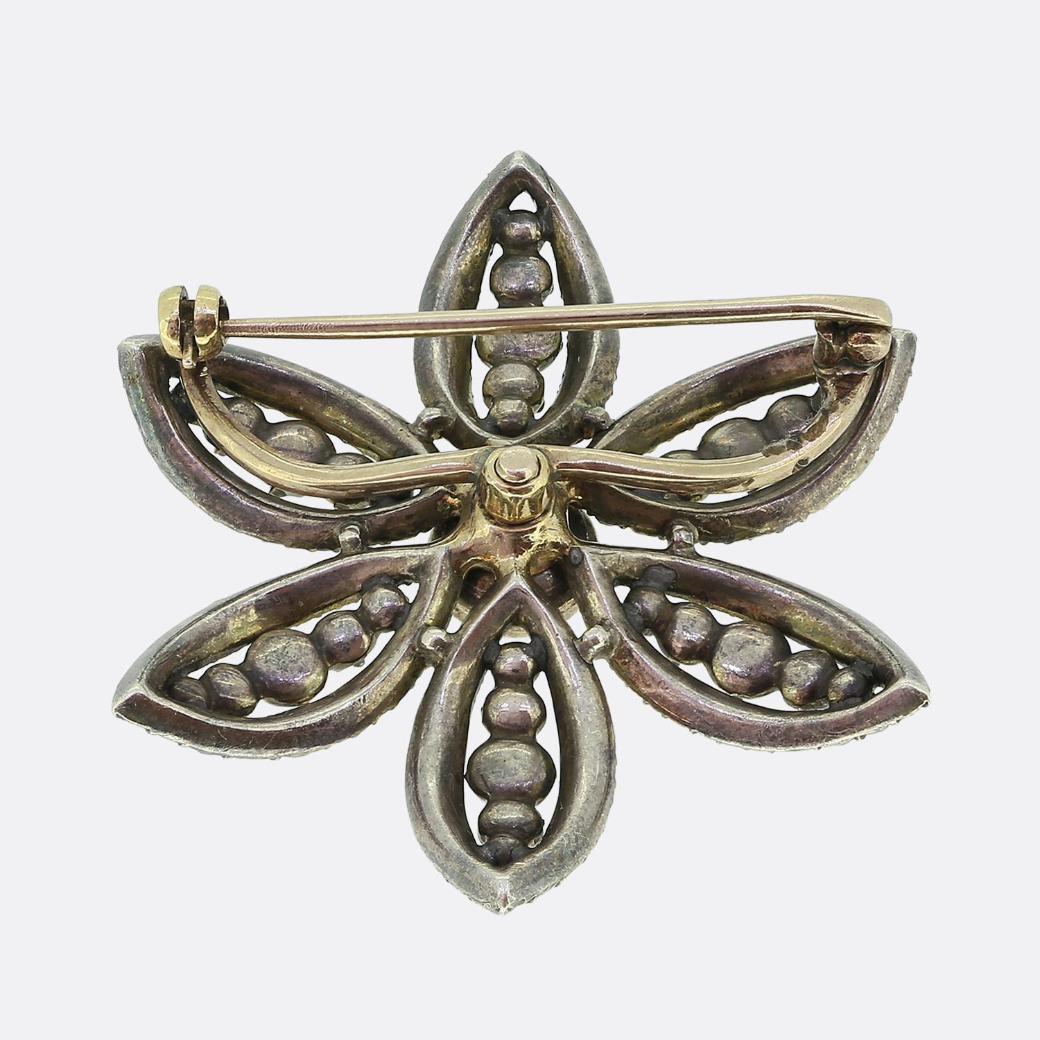 Here we have an exquisite antique brooch showcasing a floral motif, meticulously crafted with a impressive round faceted old mine-cut diamond at the centre. This principal stone, with its white hue, is surrounded by a series of smaller diamonds,
