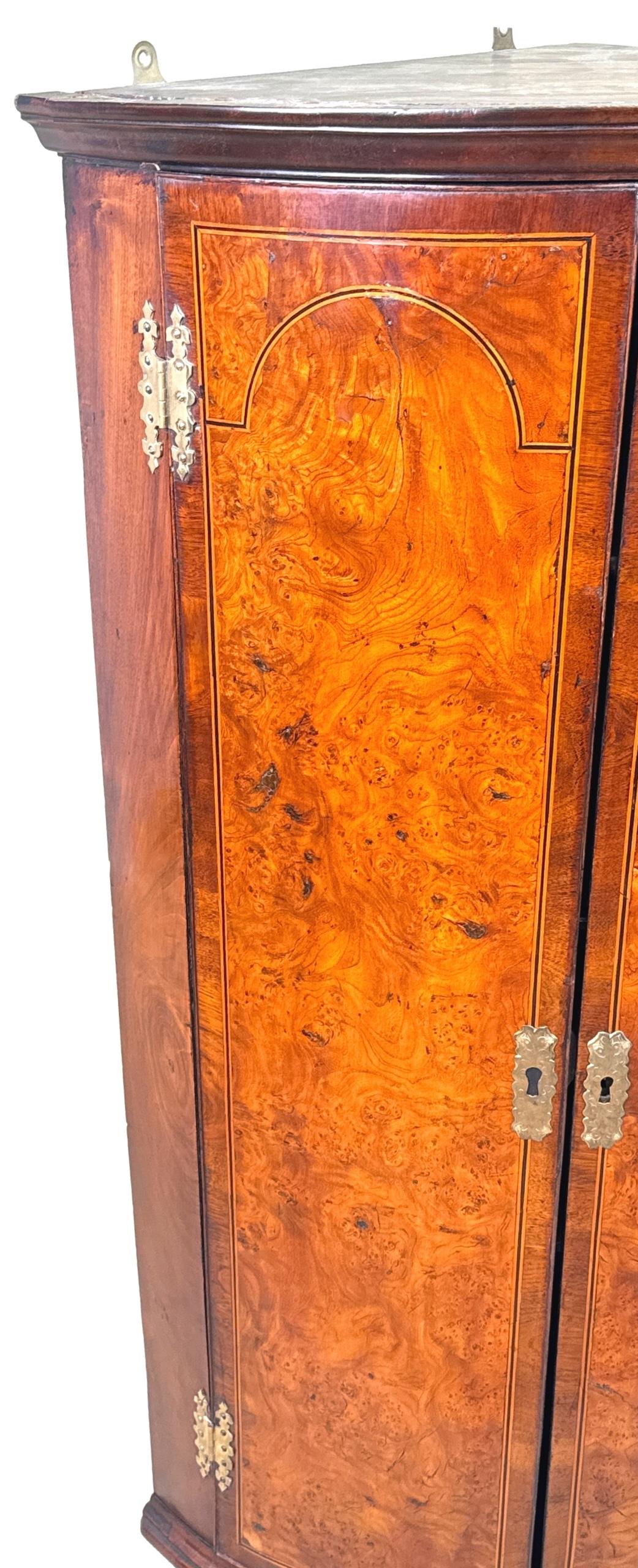 Encantador armario esquinero de madera de nogal y olmo de la época de Jorge I con frente de arco, colgado de la pared, puertas magníficamente labradas con atractiva decoración de bandas cruzadas e incrustaciones, bisagras originales de latón grabado