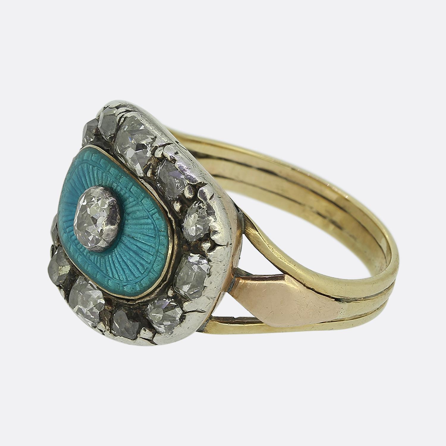 Here we have a striking cluster ring originally dating back to the Georgian period. At the centre of the face we find a captivating round faceted old mine cut diamond. This principal stone is set alone atop a vibrant turquoise coloured guilloché