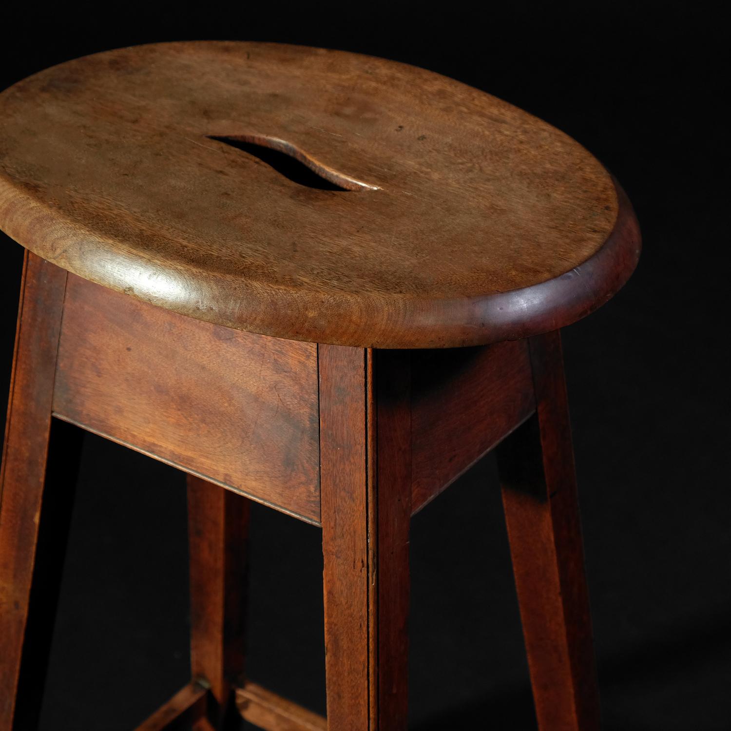 A tall Georgian stool in well patinated mahogany. Oval top with ‘s’ shape handhold, set on square-tapered legs with beaded corners and united by similar stretchers. Showing signs of age and use as expected but solid as an ox and ready to be used