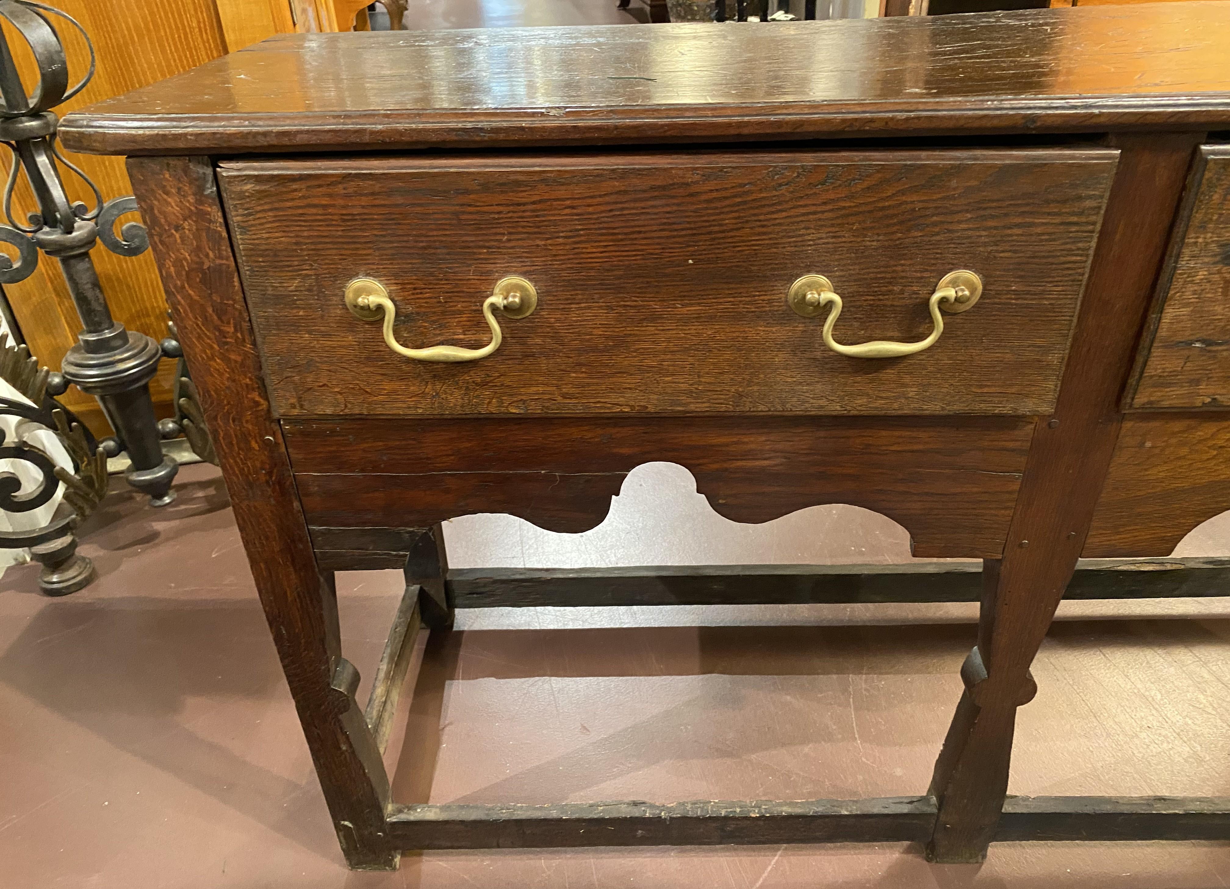 Un bel exemple de commode anglaise en chêne sculpté de la fin du XVIIIe ou du début du XIXe siècle, avec deux tiroirs encastrés dotés de cuivres d'origine et d'une jupe décorative sculptée de festons, le tout soutenu par cinq pieds (les trois