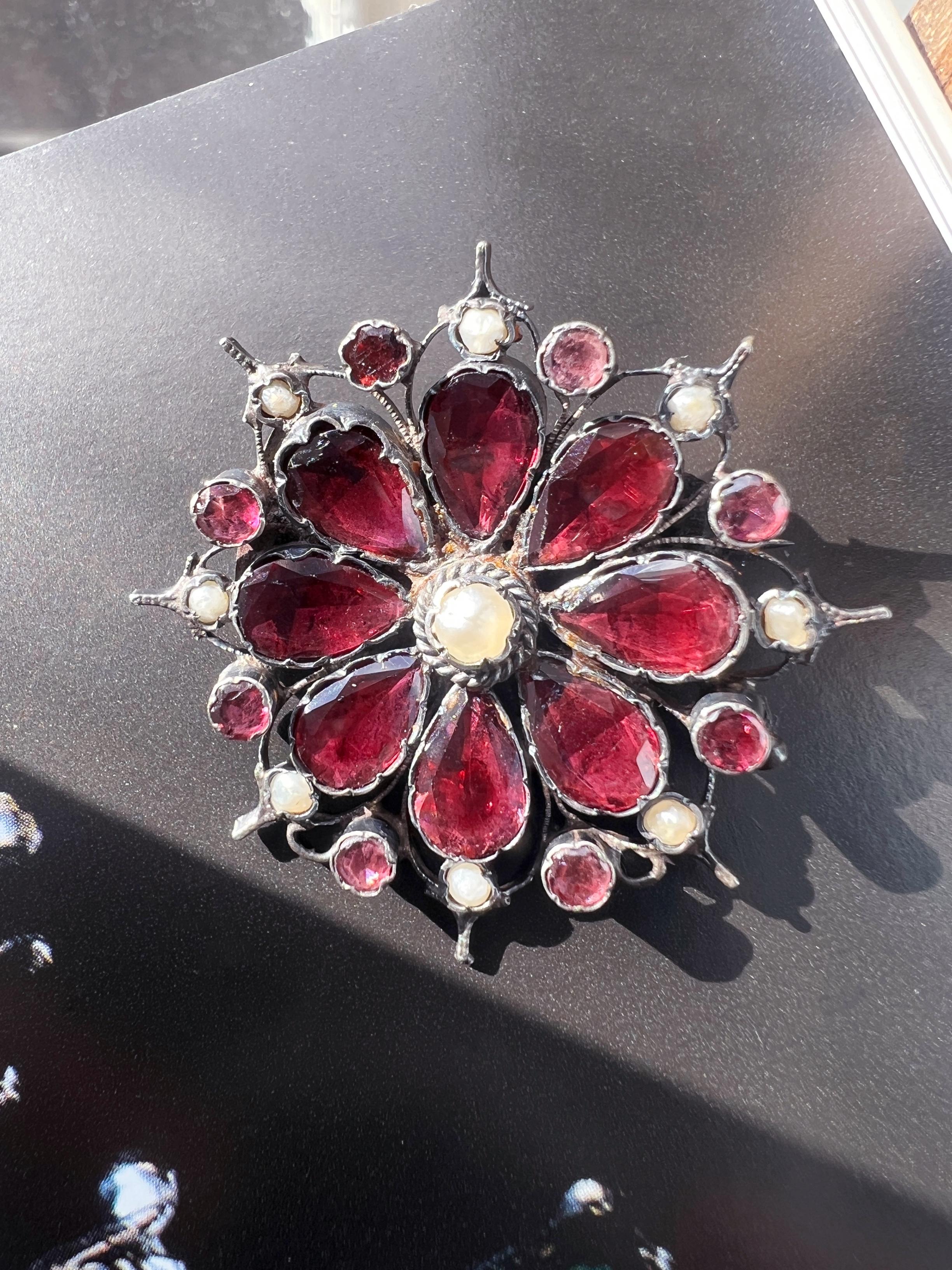 Introducing a stunning early 19th-century flower brooch. This lovely piece of jewelry features 8 delicate petals made of pinkish-red garnets, which are in flat cut style and mounted in silver with closed backings. Those characteristics are typical