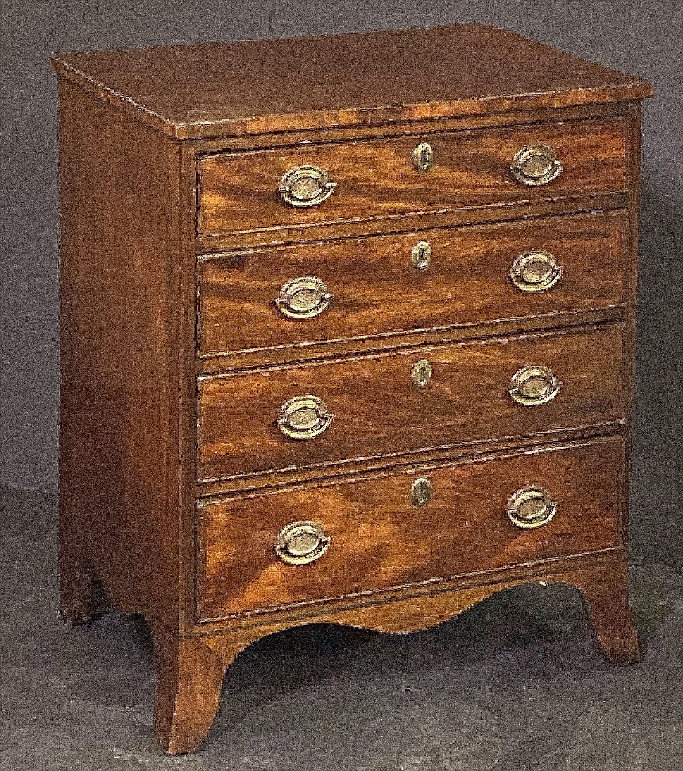 Piccola cassapanca inglese in mogano di epoca georgiana, caratterizzata da un piano sagomato su un fregio di quattro cassetti con tiretti ovali in ottone, ogni cassetto con scudetto in ottone, e posta su un grembiule a serpentina con piedini.
