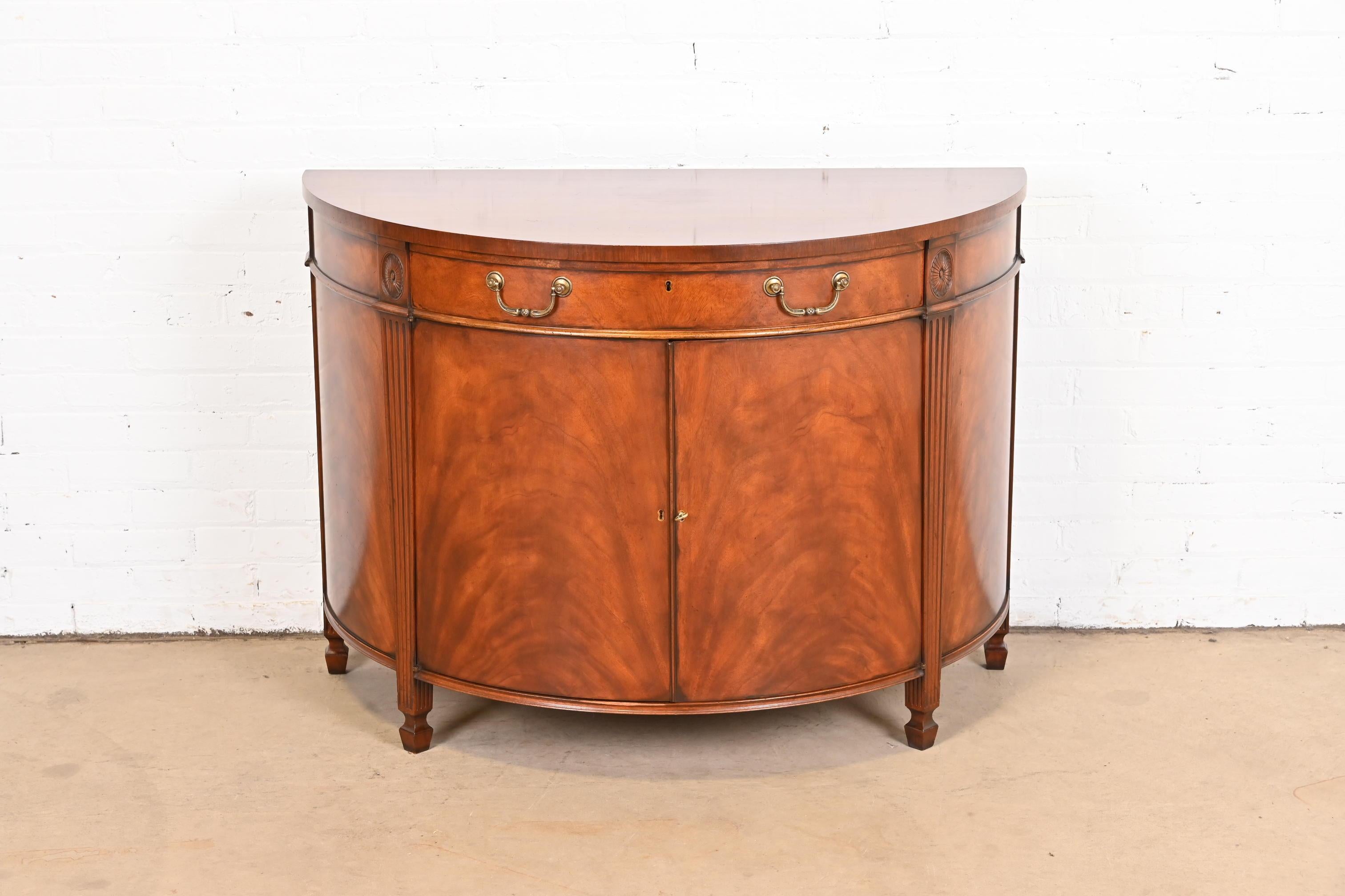 An exceptional Georgian style demilune sideboard or bar cabinet

In the manner of Baker Furniture

USA, circa 1980s

Gorgeous flame mahogany, with original brass hardware. Cabinet locks, and key is included.

Measures: 45.25