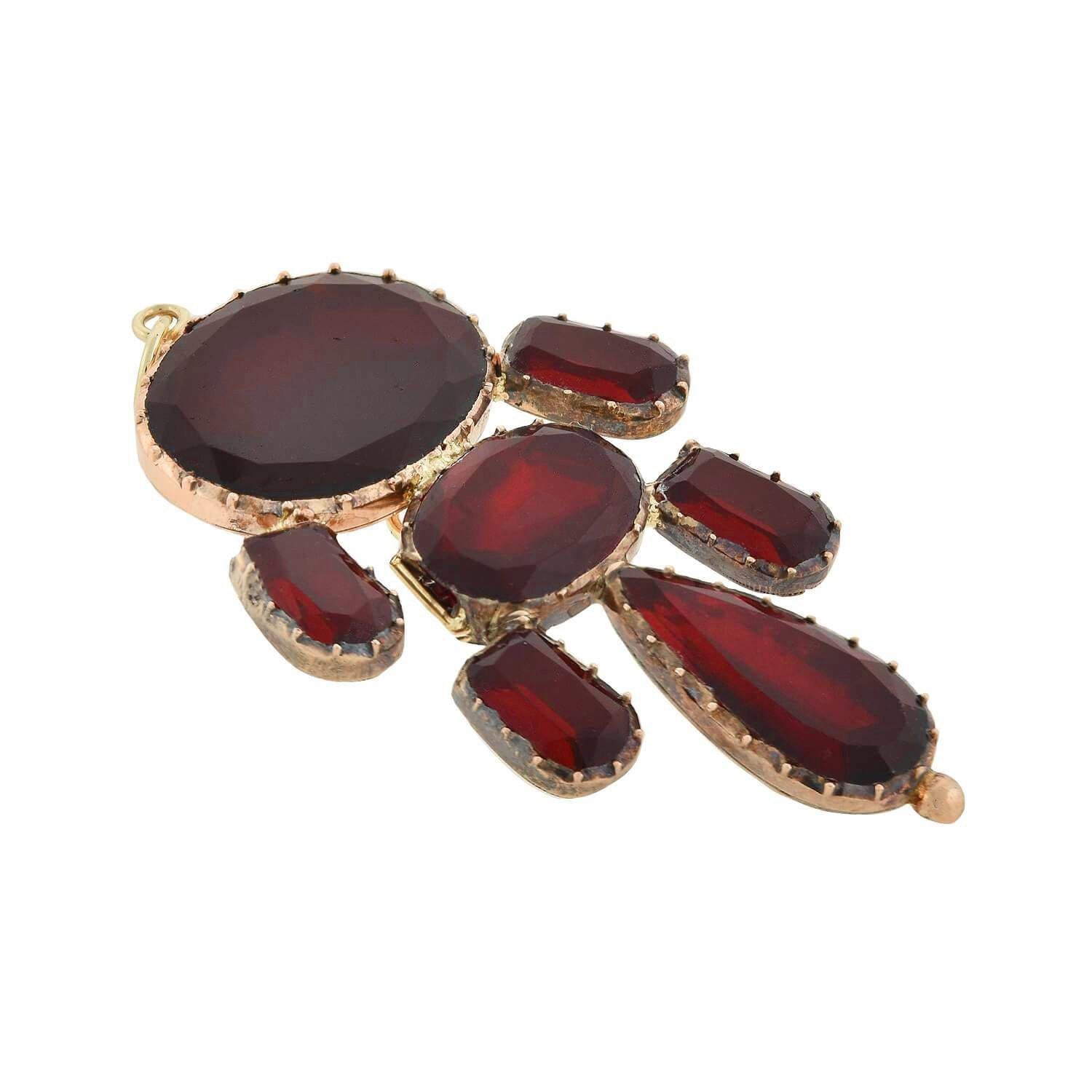 A stunning garnet pendant from the Georgian (1830s) era! Crafted in 18kt yellow gold, this beautiful piece displays seven vibrant garnets that hang from a simple gold bail in an elongated design. The garnets have a flat face with facets along the