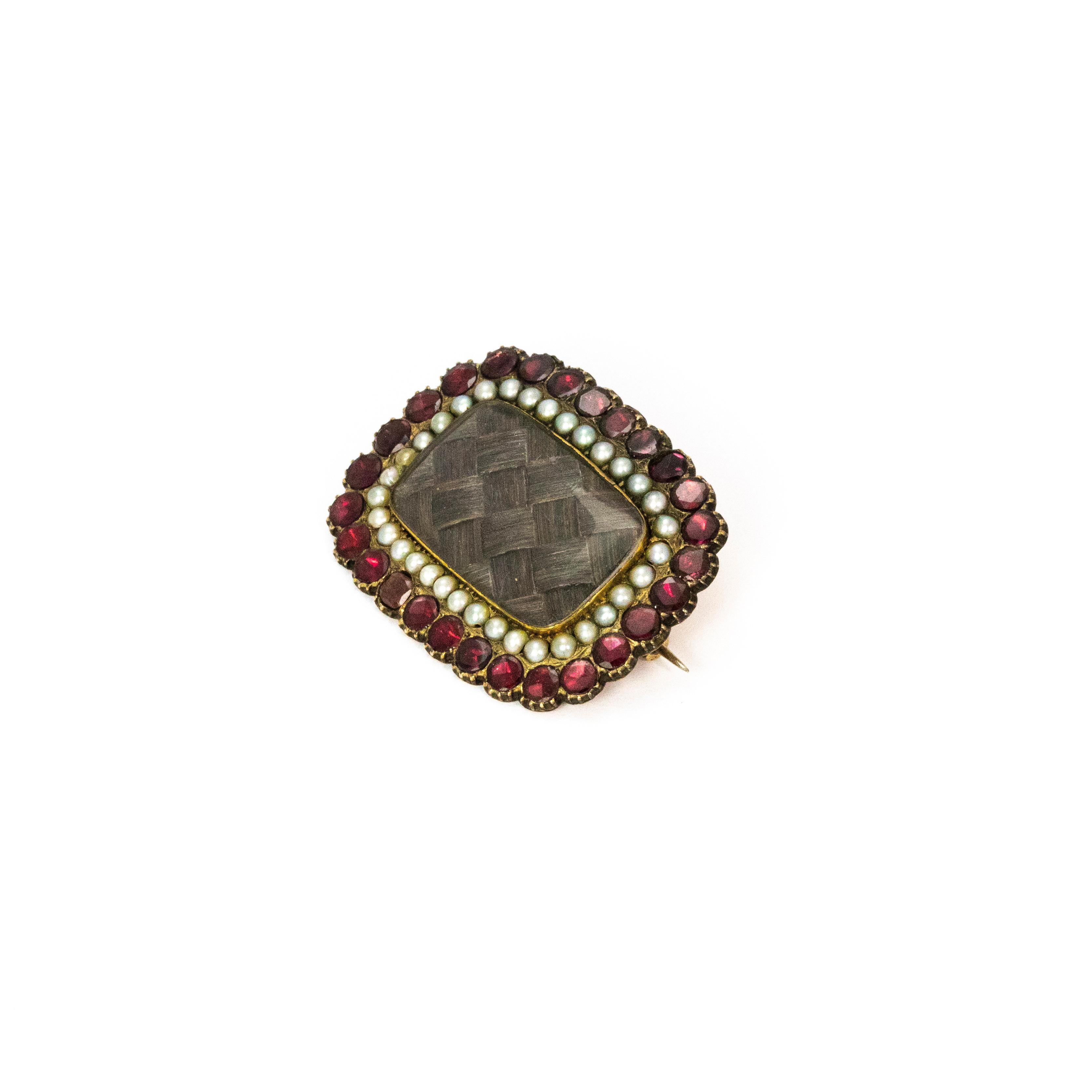 A wonderful Georgian mourning brooch. The outer edge is lined with magnificent red flat cut garnets, with an inner circuit of split seed pearls. The glazed locket centre contains the traditional woven hair of E. Brinks, the person the brooch is