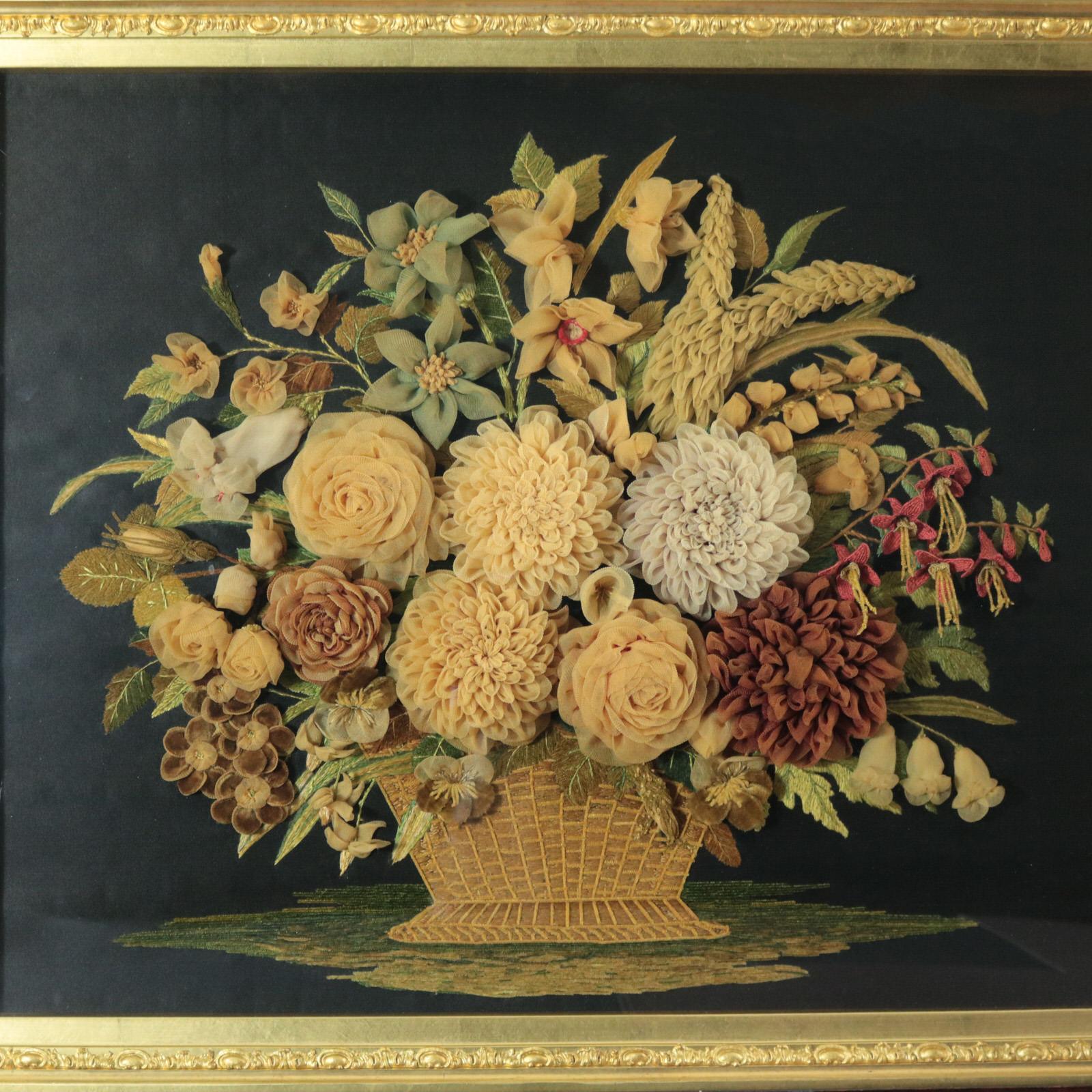 An embroidery picture of a basket of flowers. Deep relief raised work depicting leaves, twigs, flowers and grasses in a variety of techniques. The flowers are 3D, raised by about 1.5 inches. Worked in fine silks on dark linen ground, in a variety of