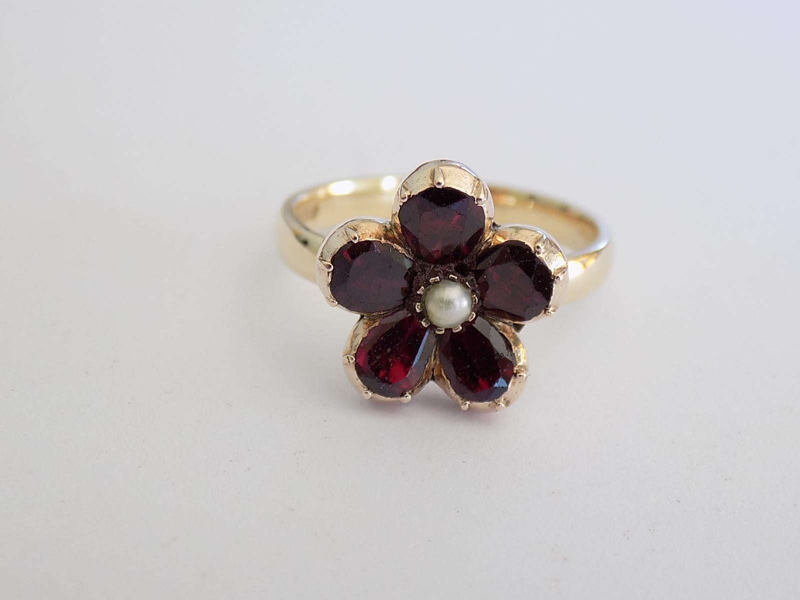 A Lovely Georgian c.1800 9 Carat Gold, Pearl and Garnet flower ring. The Garnet in foil closed back setting on later 9 Carat gold shank. English origin.
Size N UK, 7 US.
Height of the face 14mm.
Weight 3.7gr.
Hallmarked for 9 carat gold.