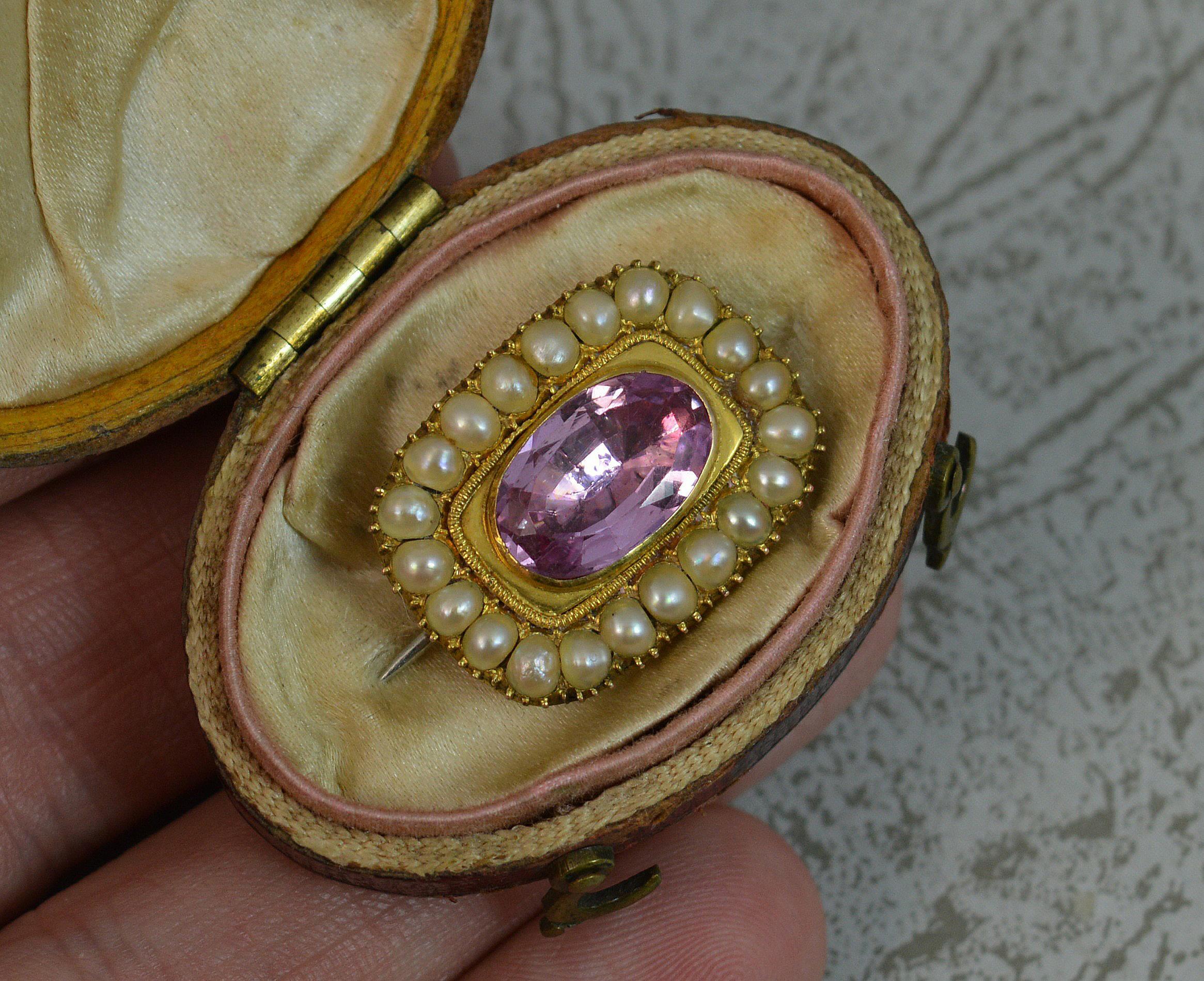 A stunning Georgian period panel brooch.
Solid 15 carat yellow gold example.
Designed with a single oval cut, closed, foiled back pink topaz to the centre. Surrounding are multiple pearls all in a closed setting.
Complete in a rouge coloured oval