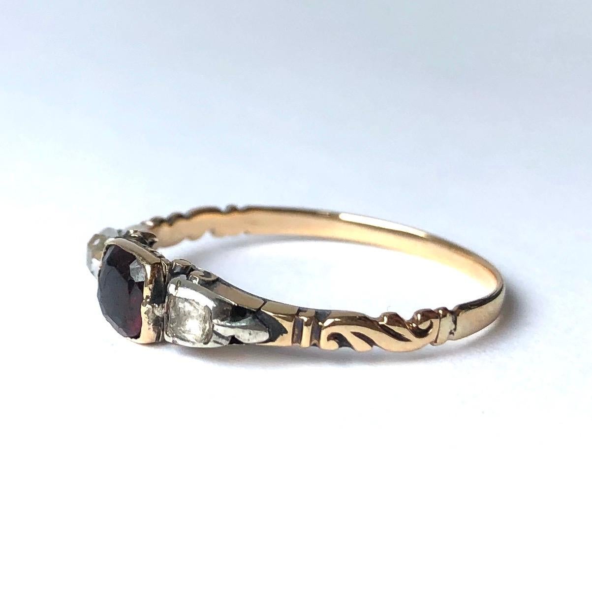 At the centre of this three stone ring there is a deep glossy red garnet and either side of this stone sits 1 rose cut diamond and one paste. The settings and shoulders are typically Georgian and the shoulders have some really lovely detail to them.