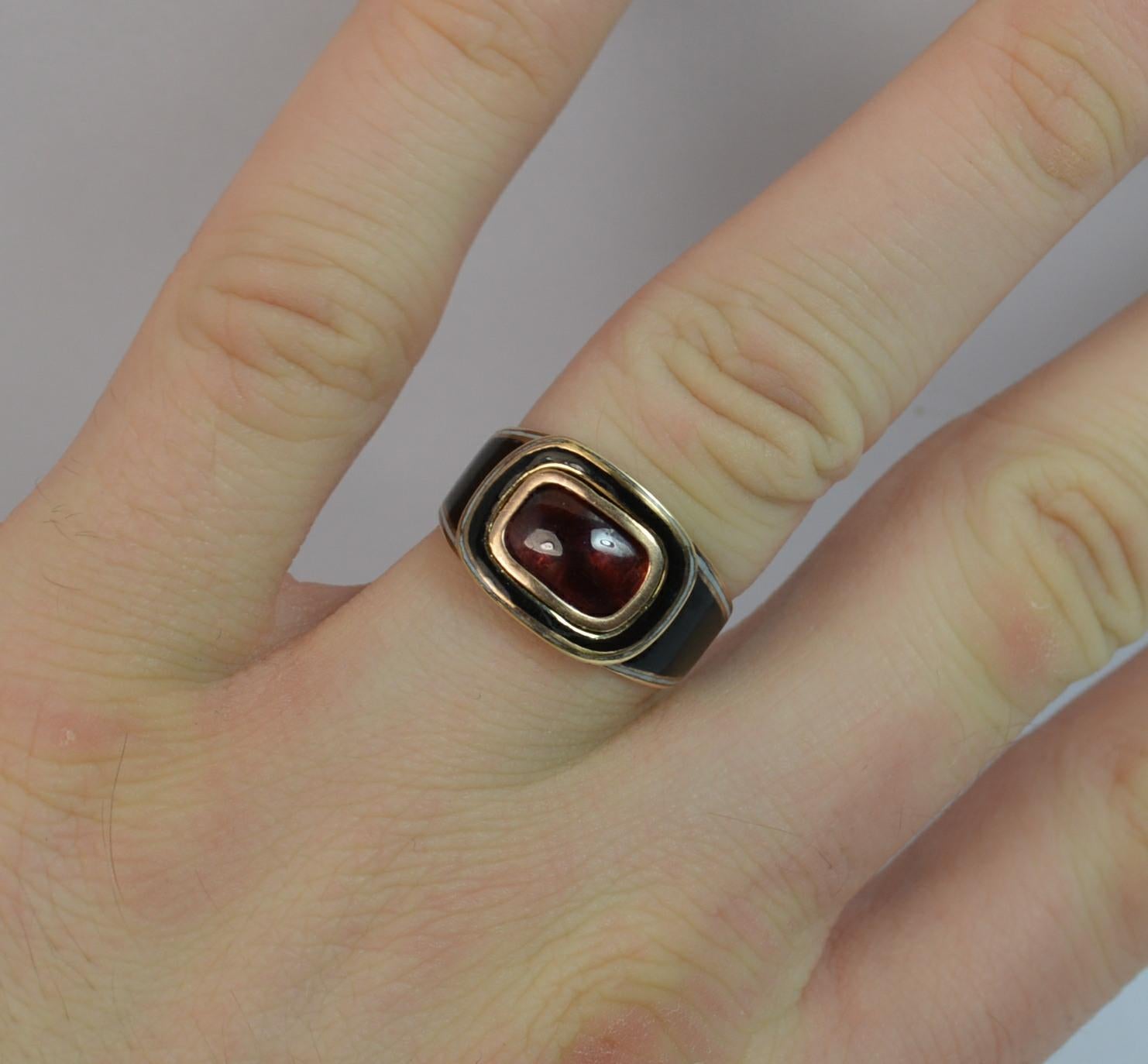 A true Georgian period mourning ring.
SIZE ; M UK, 6 US
Designed with a natural foiled back garnet cabochon to the centre and white and black enamelling surrounding and to the full band.

The head measures 15mm x 11mm approx.



CONDITION ; Very