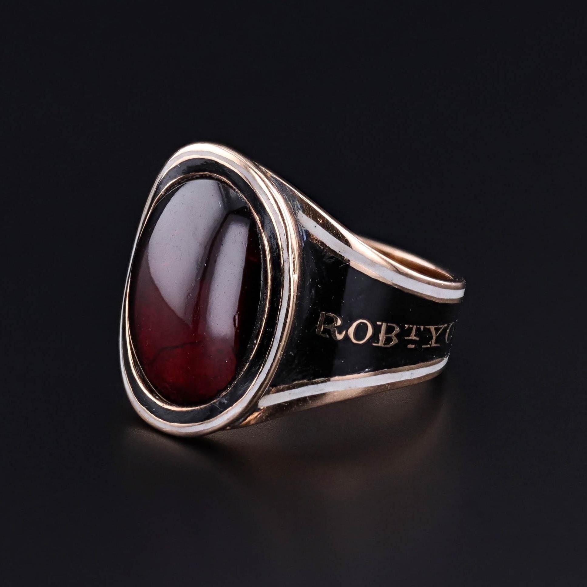 Antique Garnet Mourning Ring: This antique mourning ring dates to the Georgian era and features a large garnet cabochon set in 18k gold. The band is adorned with white and black enamel and is engraved with a memorial inscription 'RobT