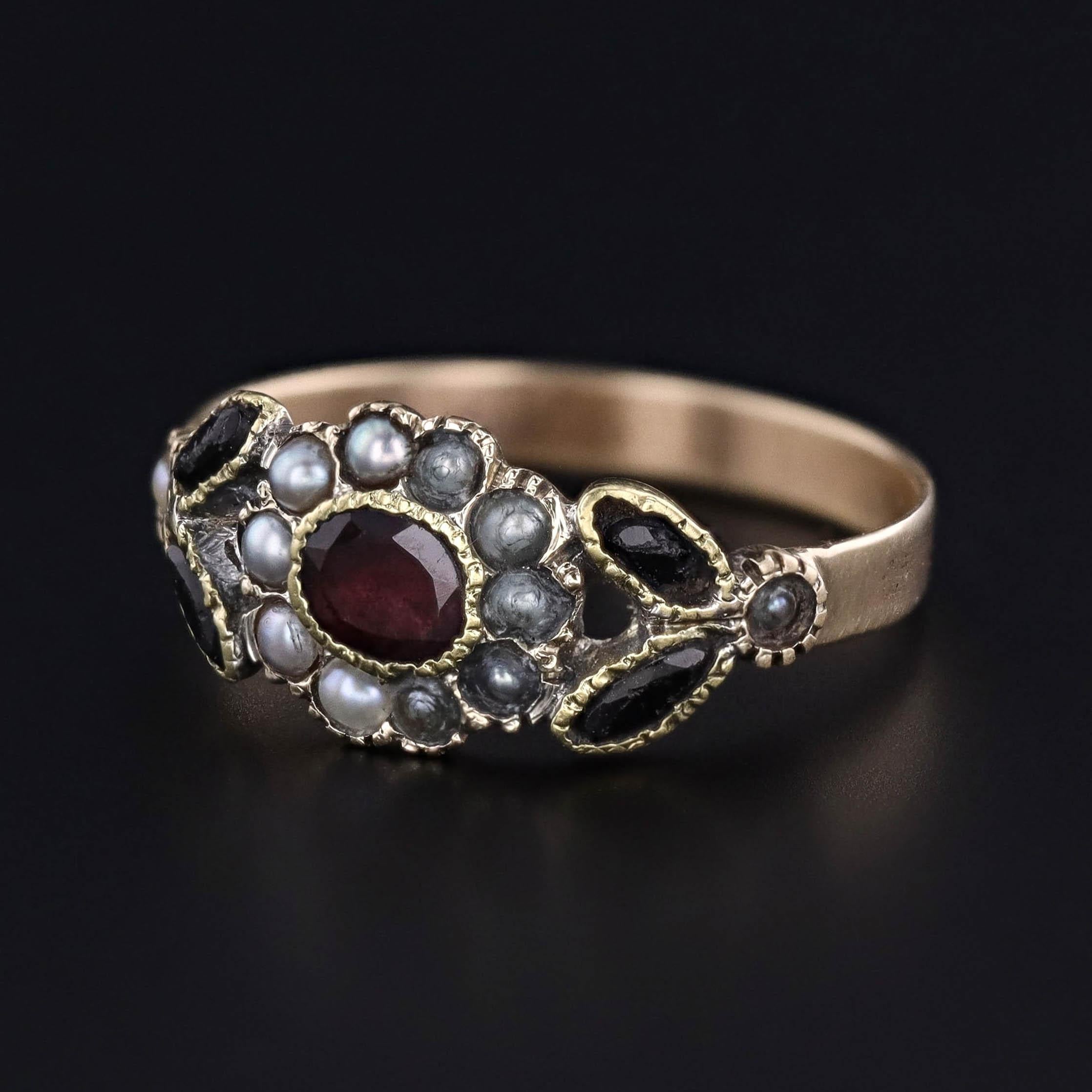 A Georgian era ring (circa 1830) featuring a flat cut garnet surrounded by split pearls and onyx accents set in 14k gold.

The face of the ring measures 0.3 inches from north to south and is in fair condition with some nacre loss to a several pearls