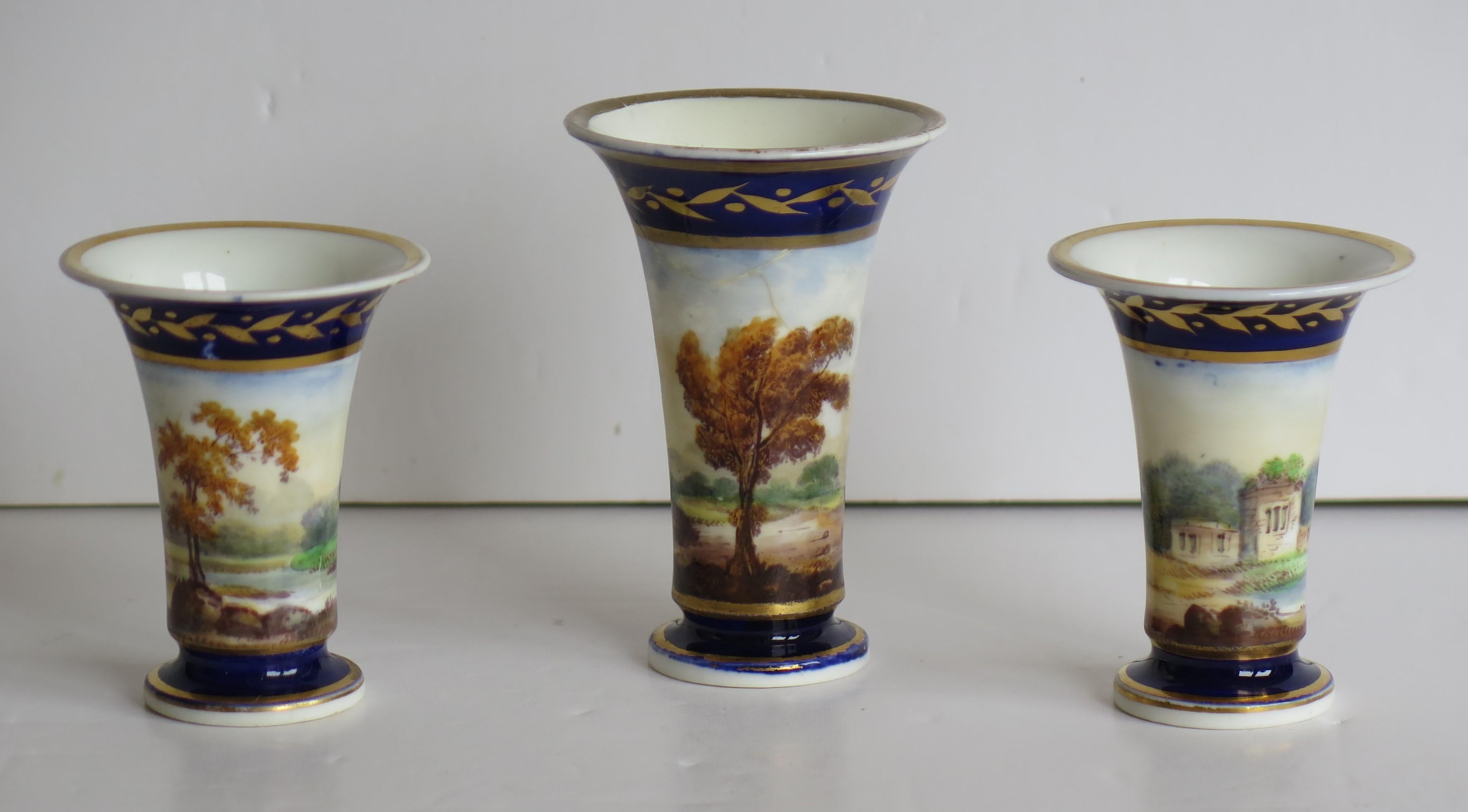 These are a very good example of a Staffordshire porcelain Garniture set of Three Miniature Vases, all finely hand painted and gilded in English landscape scenes, and dating from the early 19th century, circa 1820.

These are a high quality set of