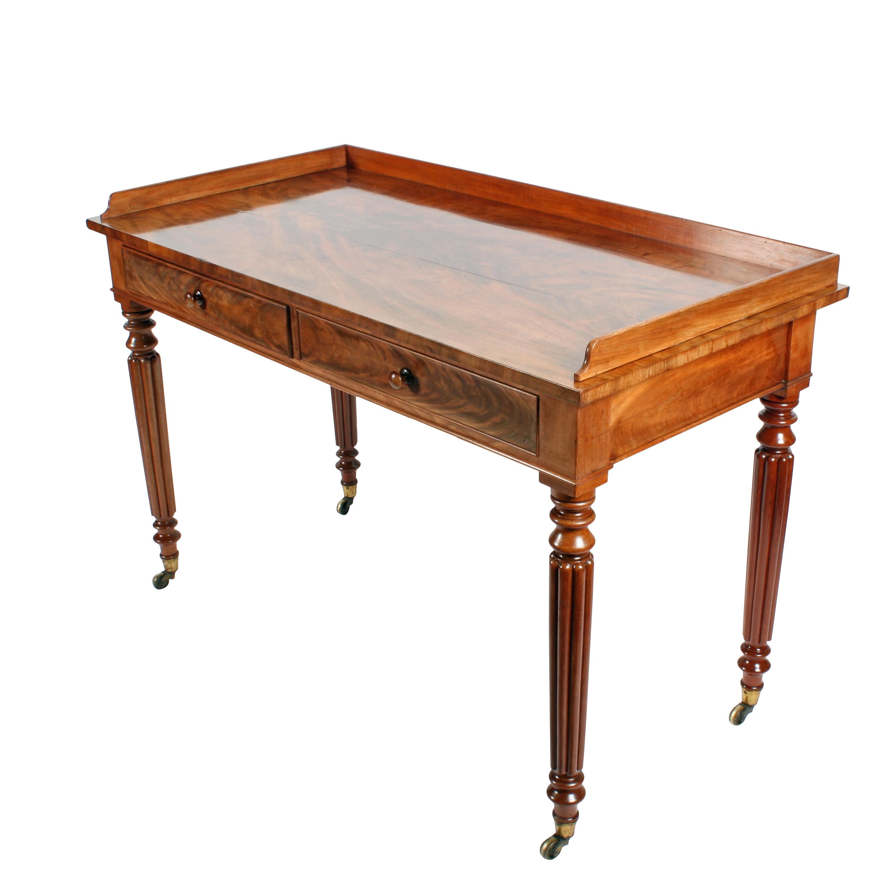 An early 19th century Georgian mahogany two-drawer side table.

The table is in the style of 'Gillows of Lancaster' with a gallery back and four turned tapering and reeded legs that have gilt brass casters.

The drawers are mahogany lined with