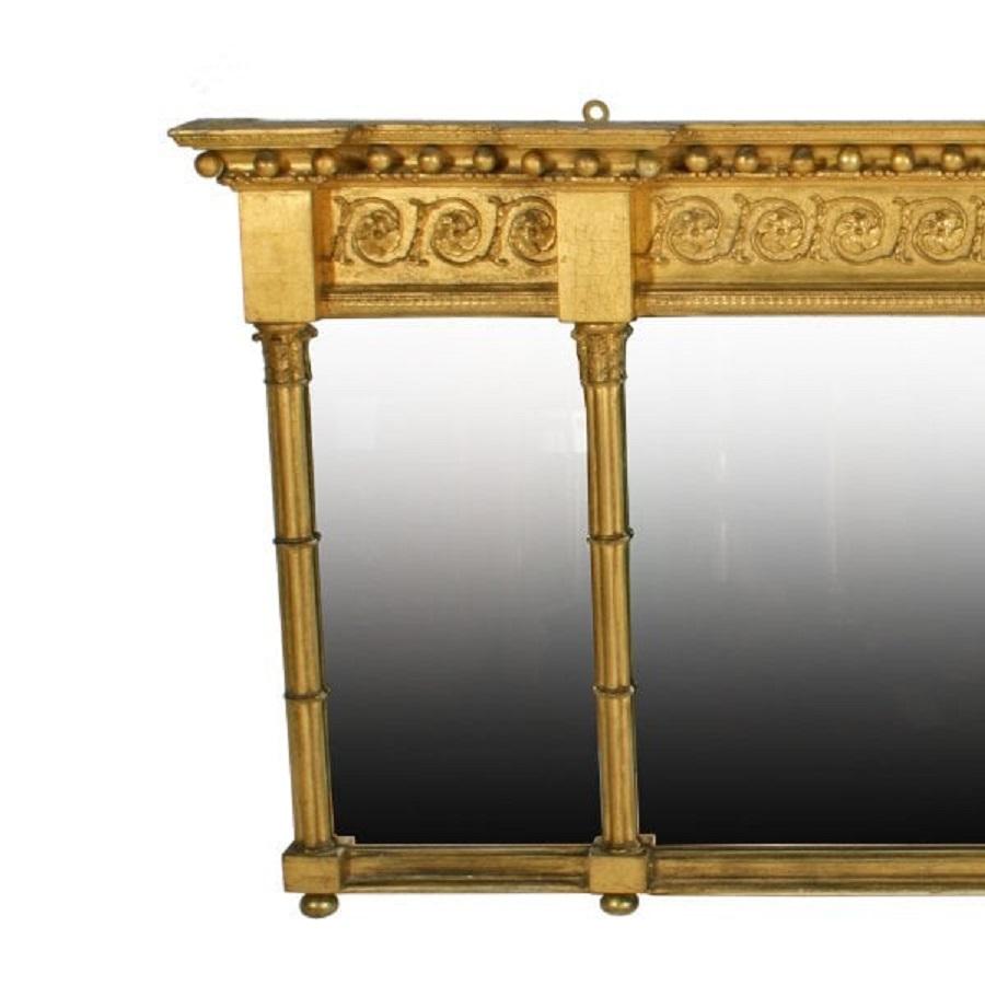 An early 19th century Georgian gilt wood and gesso overmantel mirror.

The mirror has an overhanging cornice decorated with gilt wood balls above a frieze of gilt flowers and scrolls.

The frame holds three mirror plates flanked with cluster