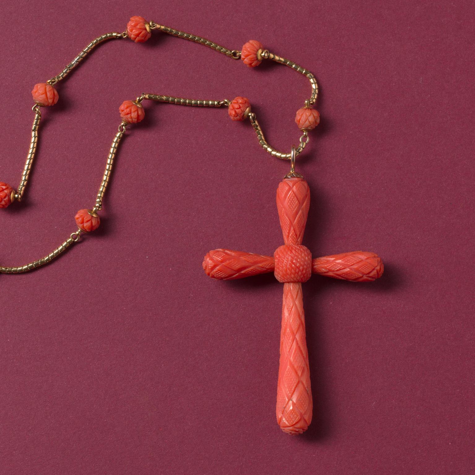 Une chaîne en or 15 carats avec 11 perles de corail sculpté et un grand pendentif en forme de croix en corail composé de cinq éléments en corail sculpté, vers 1830, d'origine anglaise.

poids total : 25,79 grammes
longueur de la chaîne : 42