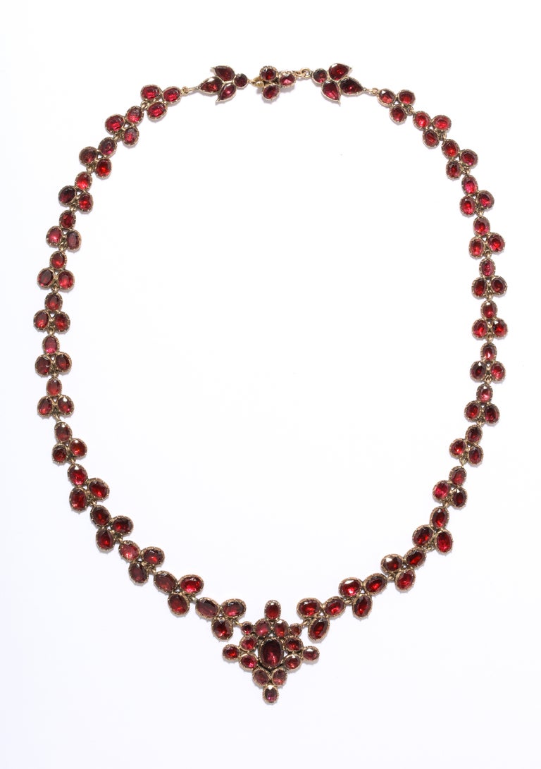Forget-me-nots drape the neck to light the day for the next owner of this perfect 15 Kt gold foiled garnet necklace dated c. 1820. At center gleams a floral medallion in varied cuts of garnets. The uniformity of the light catching port color proves