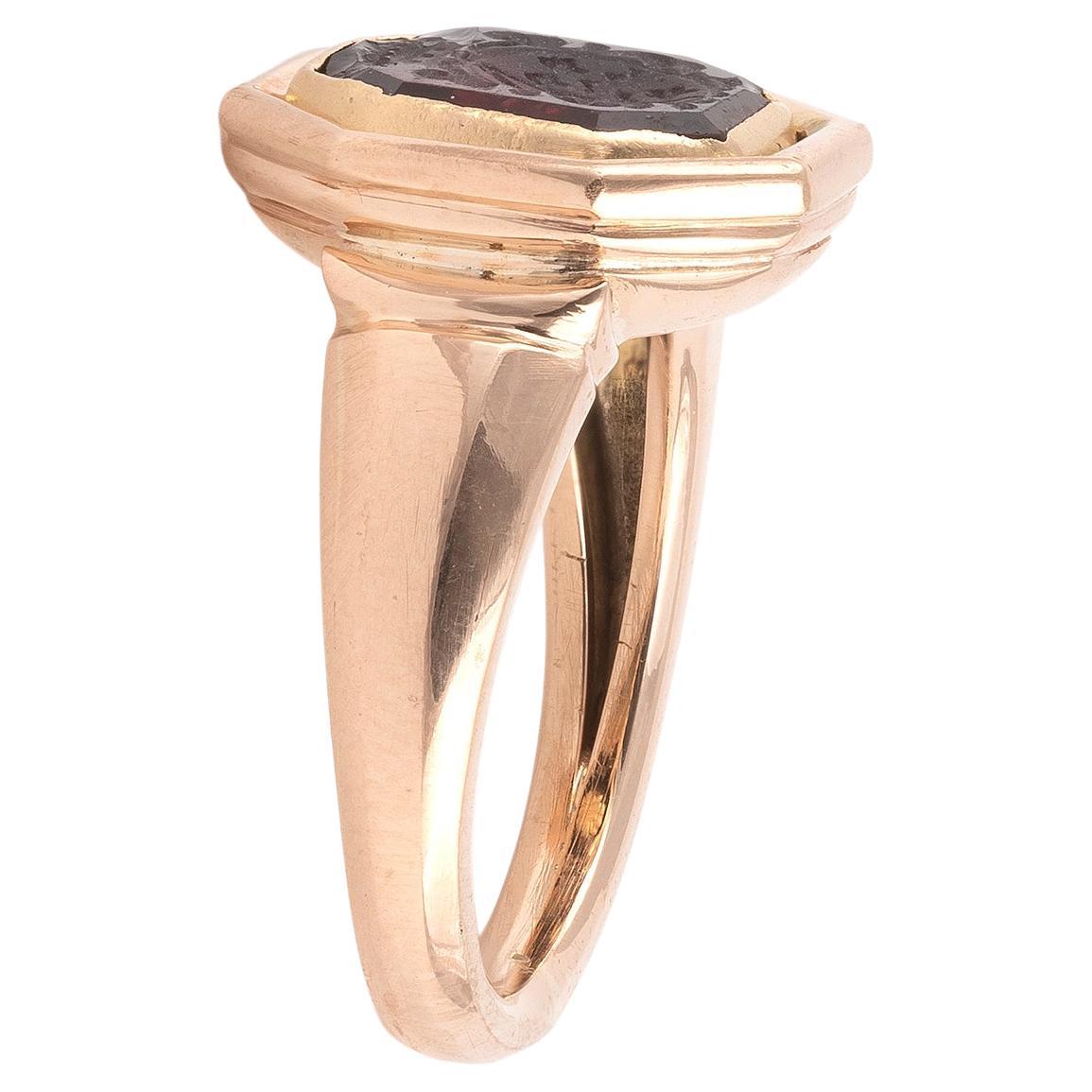 A rectangular cut cornered garnet matrix, intaglio engraved with a coat of arms, with a coronet of pearls above, possibly a Viscount's coronet. Top size 15mmx 14mm.A plain gold mount ring.
Size 7 1/4
Weight: 8.87gr