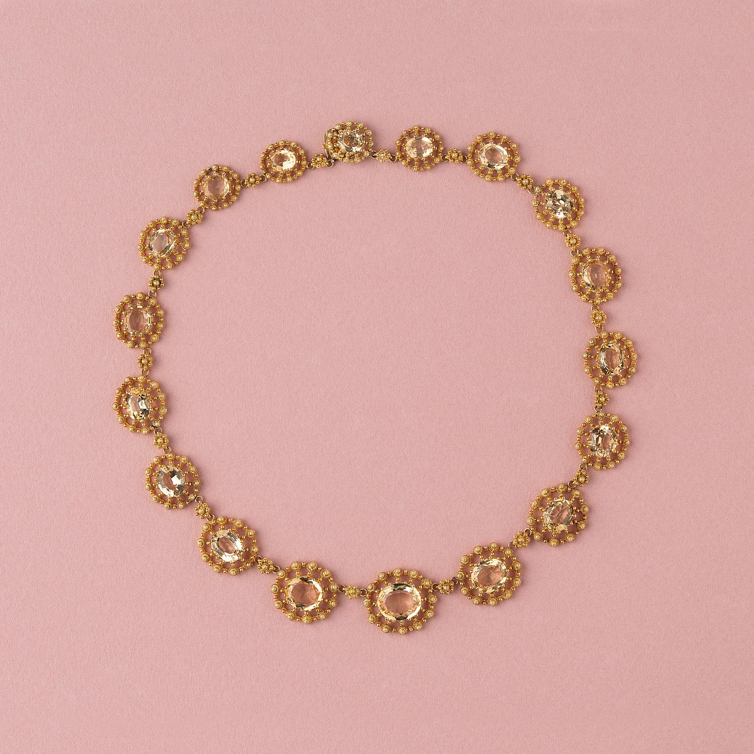An 18 carat gold elegant Georgian necklace set with 18 graduating oval facetted oval topazes each richly decorated with cannetille and granulation, France circa 1840.

gewicht: 32.59 gram
lengte: 39 cm.
breedte: 12 – 20 mm.