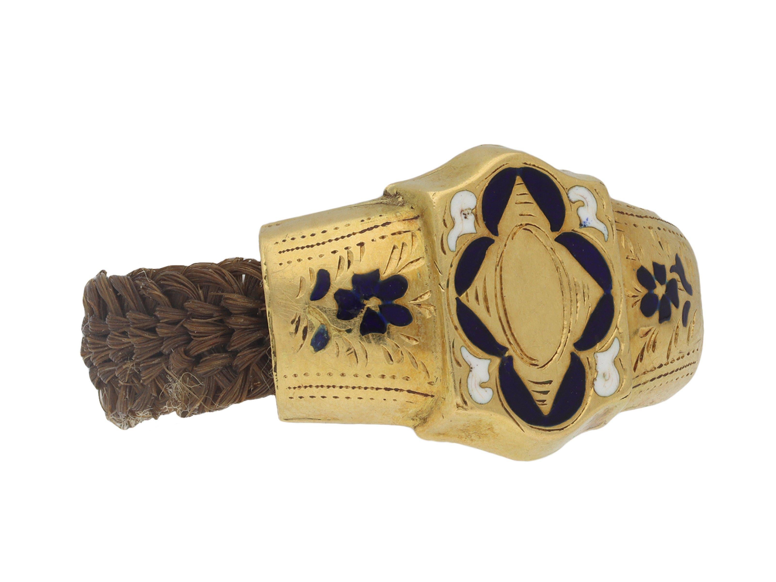 Georgian hair ring. Set with a yellow gold shield shape plaque to centre with blue enamel frame and white enamel to the corners around an engraved central circular motif, flanked by heavy tapered yellow gold shoulders with blue enamel flowers and