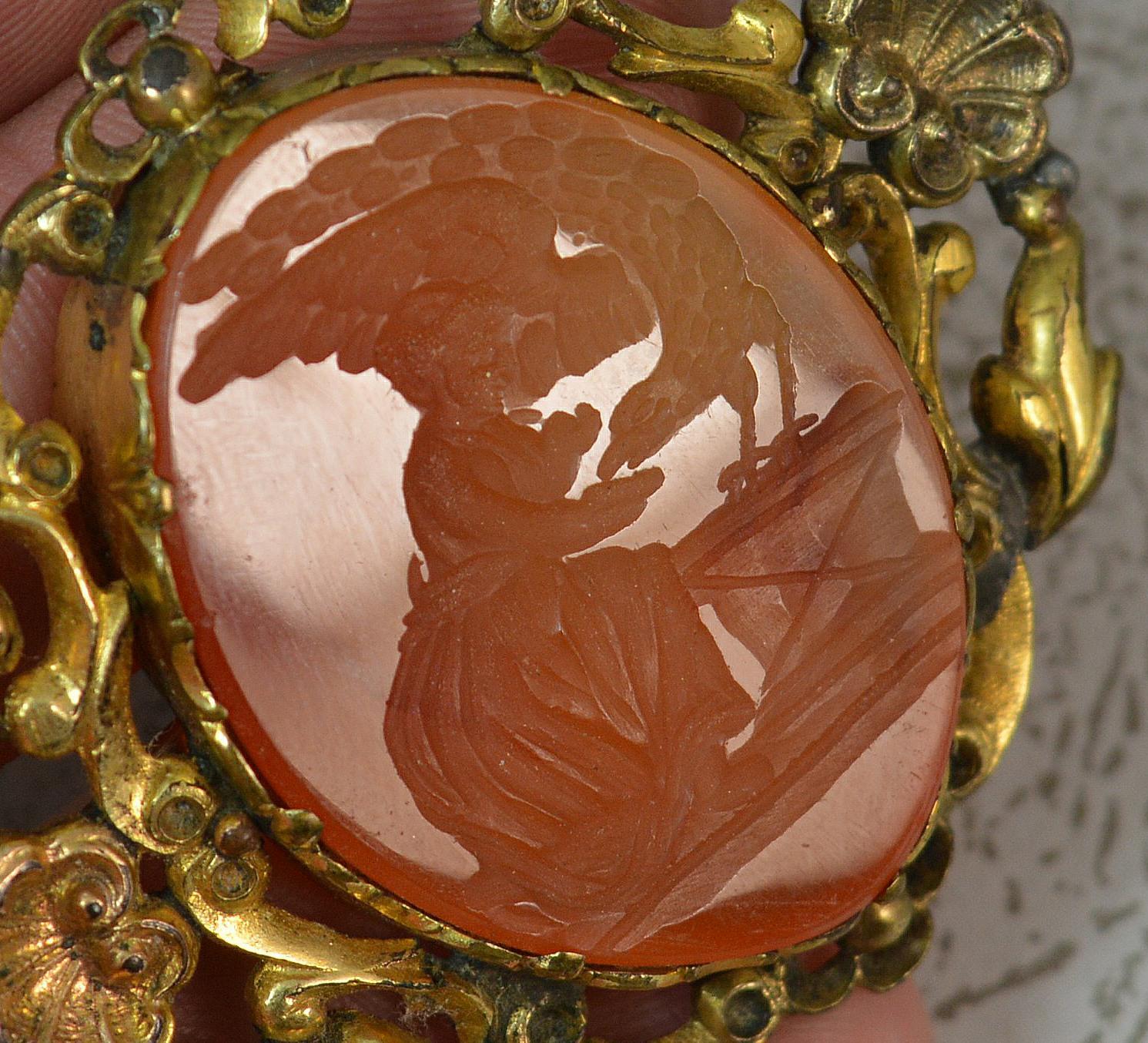 
A fine Georgian era intaglio brooch.

Large oval carnelian agate panel to centre depicting Hebe and Zeus,

Surrounded by a gold cased floral and shell design.


Condition ; Good for age. Well set stone. Very crisp, clean intaglio. Working pin and
