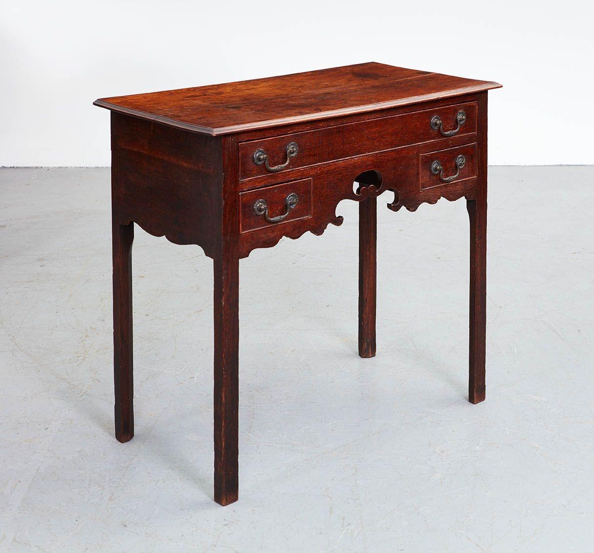 An 18th century English oak three drawer side table or lowboy, having two plank molded edged top over one long and two lower drawers all with original gilt lacquered brass bail handles, flanking a richly scalloped 
