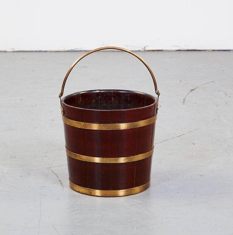 A period Georgian oak and brass peat bucket of coopered and banded construction with well patinated mahogany staves and striking contrasting brass bands fastened with brass pins.  Also featuring a brass swing handle with shaped hinged escutcheons. 