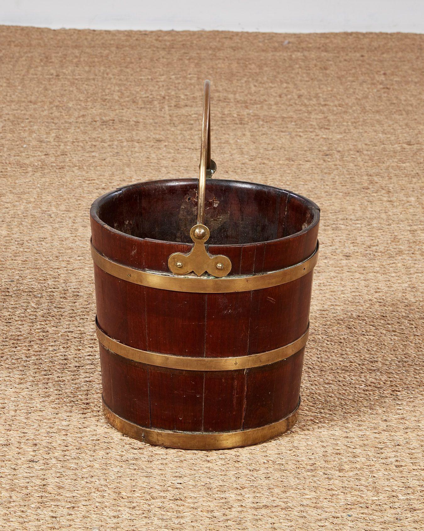 A good quality mahogany peat bucket of coopered construction bound by brass bands, with brass swing handle attached to elegantly shaped hinges.  Now useful as a kindling bucket next to a fireplace.