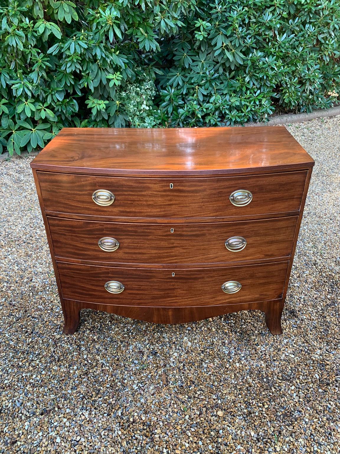 Georgian mahogany bow fronted chest of drawers with three long oak lined drawers, oval brass handles and splayed feet.