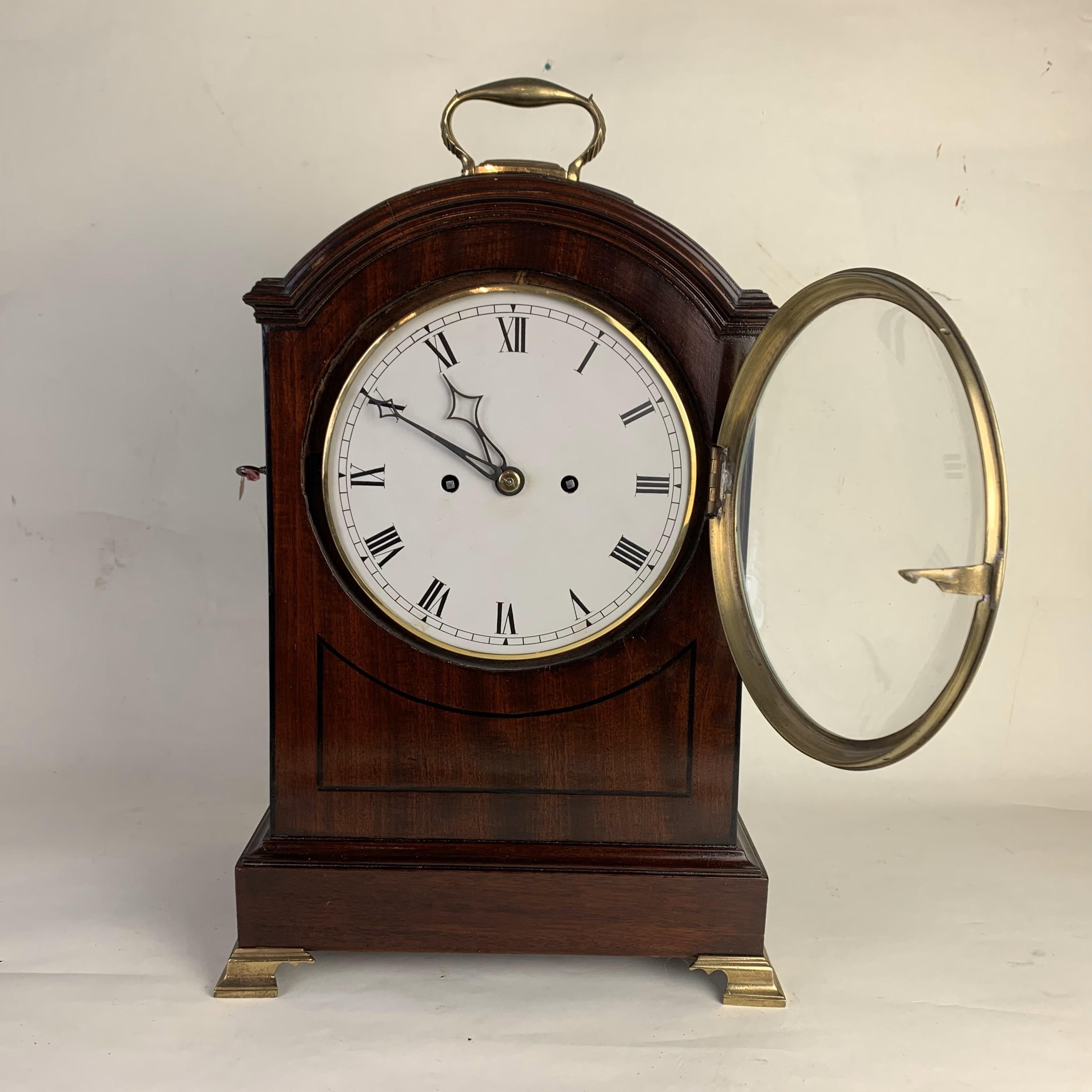 An attractive early 19th century mahogany cased bracket clock with black line inlay to the case and raised on brass ogee bracket feetand with brass carrying handle. The twin train 8-day movement chiming the hours on a bell with a white enamel dial