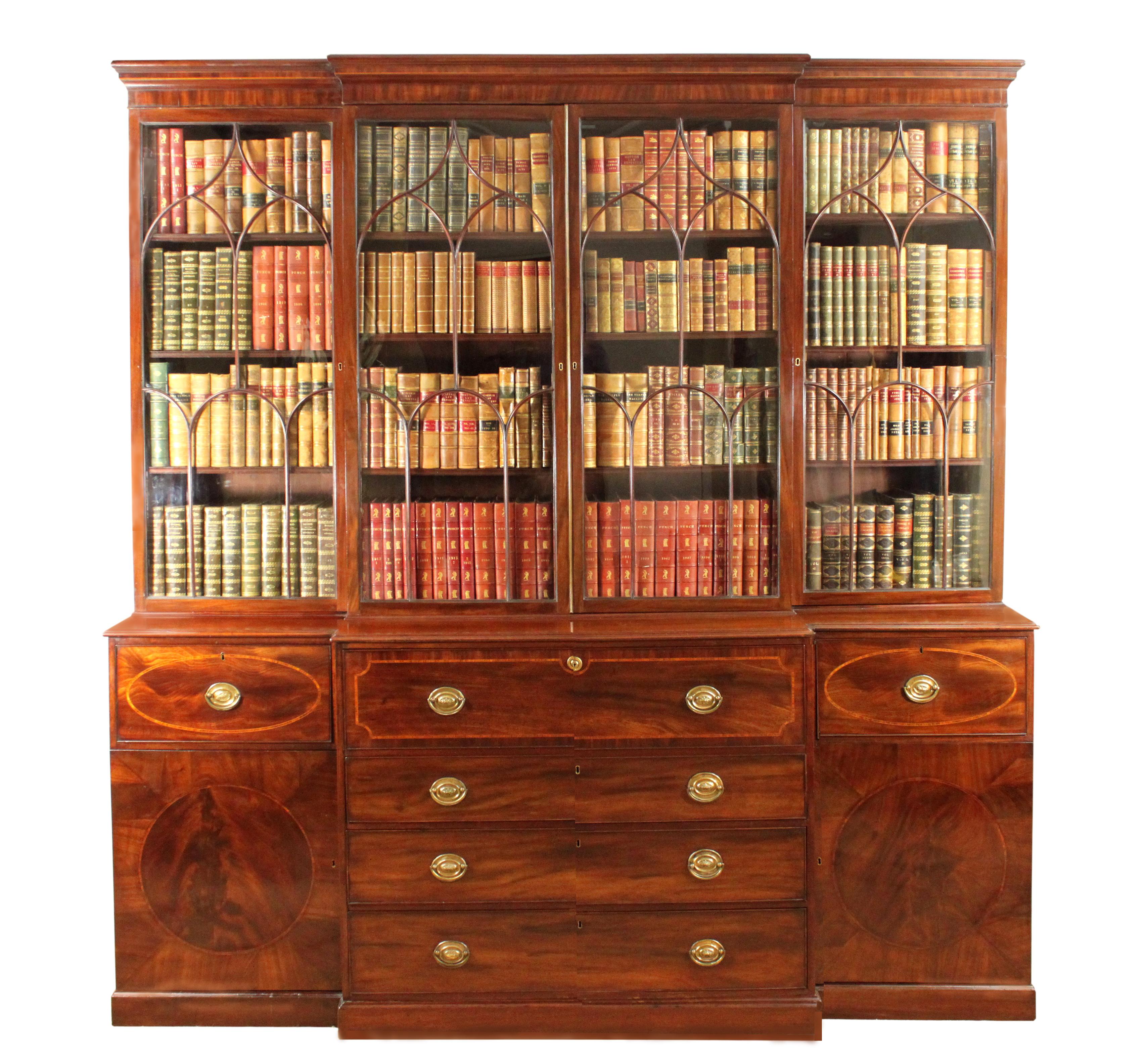 A fine George III Sheraton period mahogany breakfront bookcase with a well fitted secretaire drawer; arched glazing bars complete with the majority of the original glass. The base with attractive oval inlaid drawers and circles in the doors.