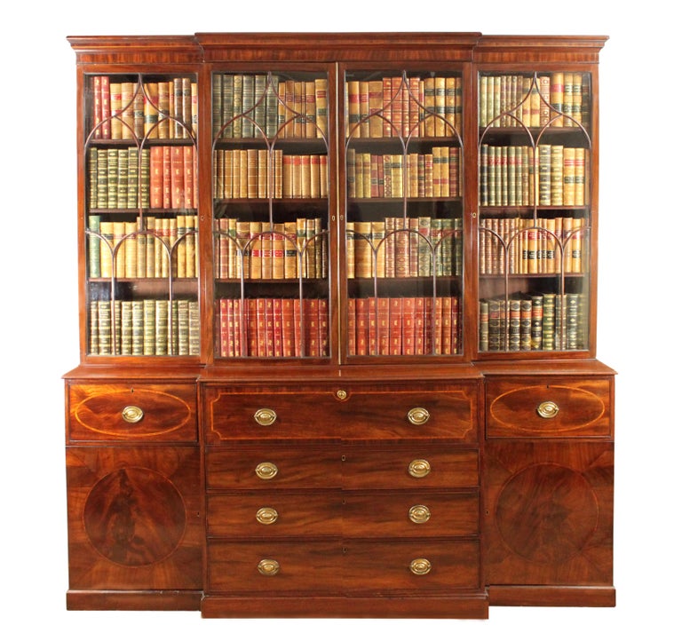A fine George III Sheraton period mahogany breakfront bookcase with a well fitted secretaire drawer; arched glazing bars complete with the majority of the original glass. The base with attractive oval inlaid drawers and circles in the doors.