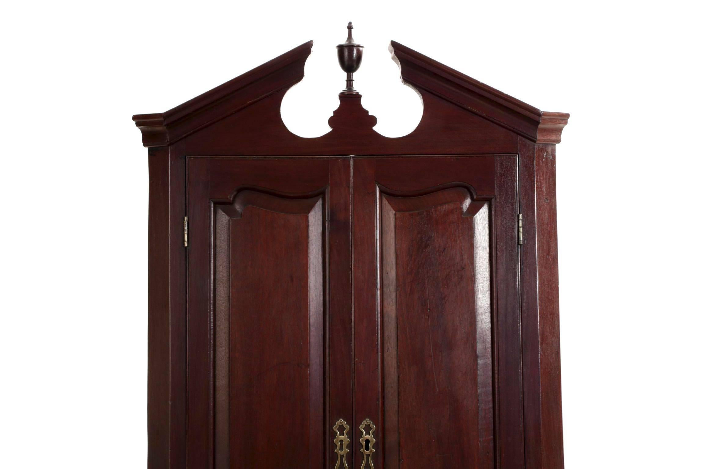 A most attractive hanging corner cupboard, it displays with a most attractive angularity emphasized by the cove-molded broken-arch crest flanking a single turned finial raised on an integral plinth. The sides of the case bevel to visually soften the